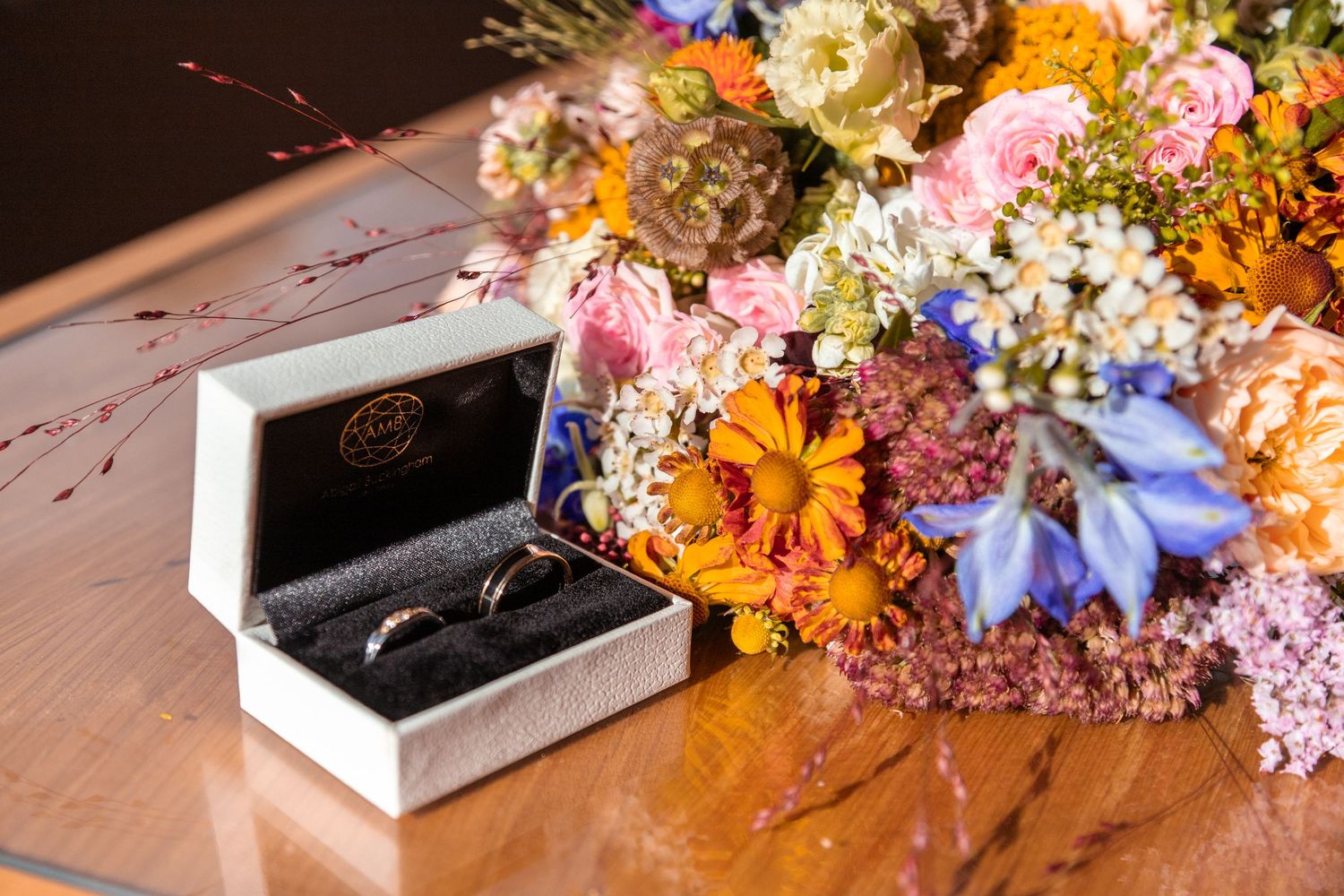 Wedding rings in box beside colorful wildflower bouquet on wooden table.
