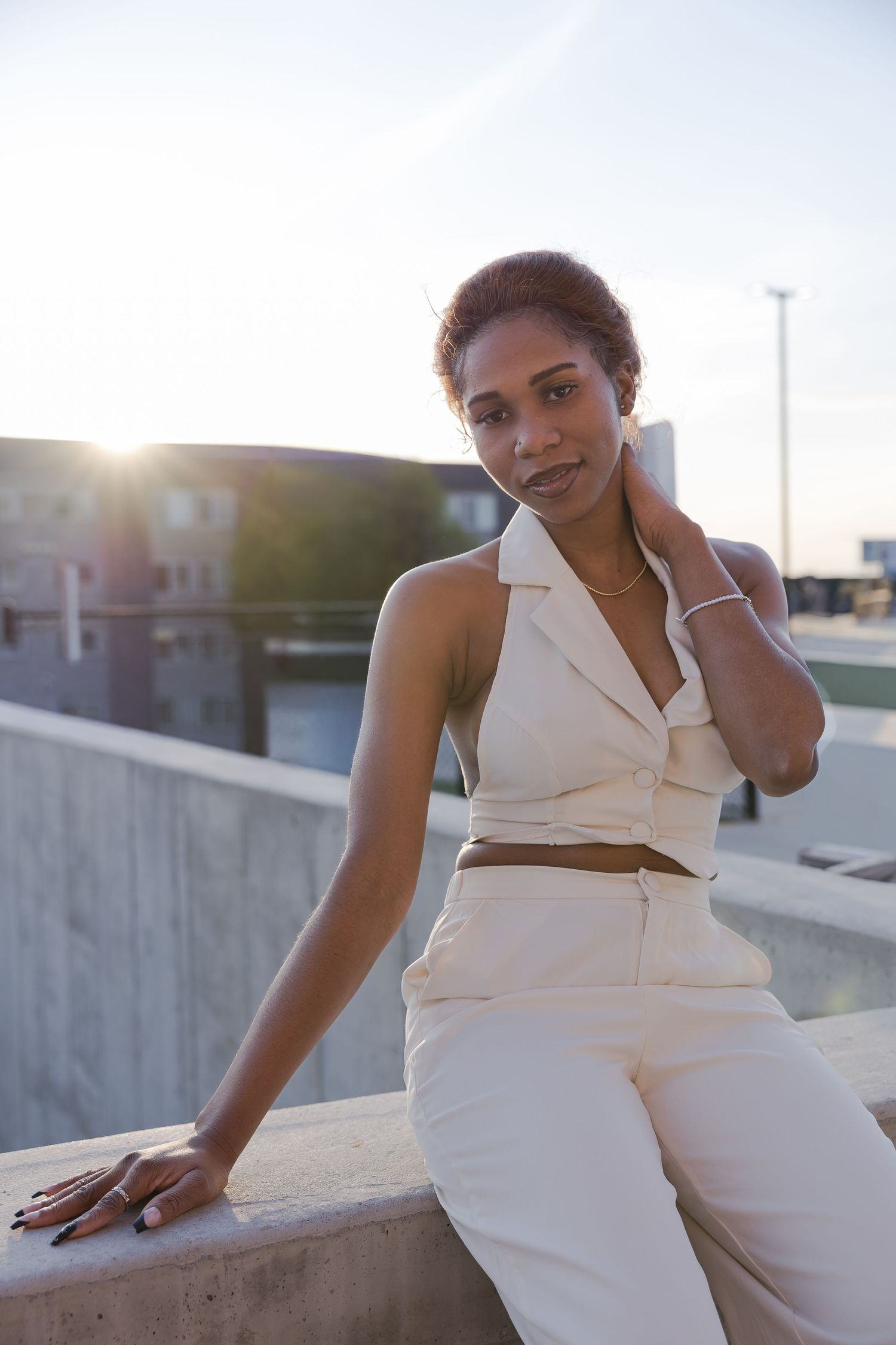 Sioux City, Iowa photographer. A young woman in a white halter outfit sits on a concrete ledge with a glowing sunset behind her.