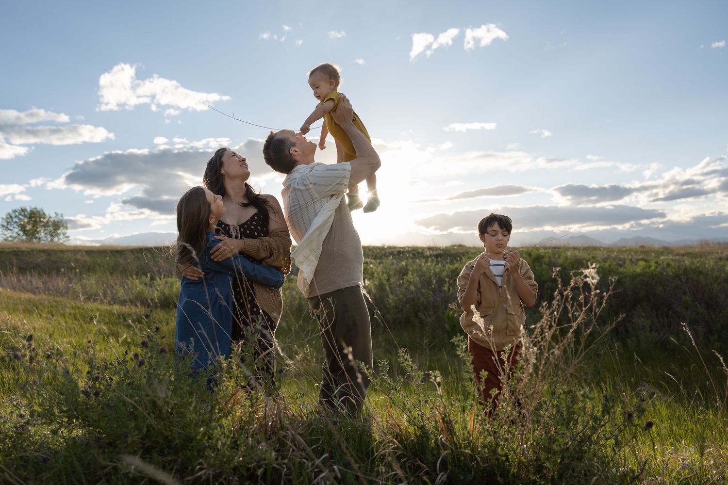 Family enjoying a sunny day in a green field, parents lifting baby while older child plays nearby.