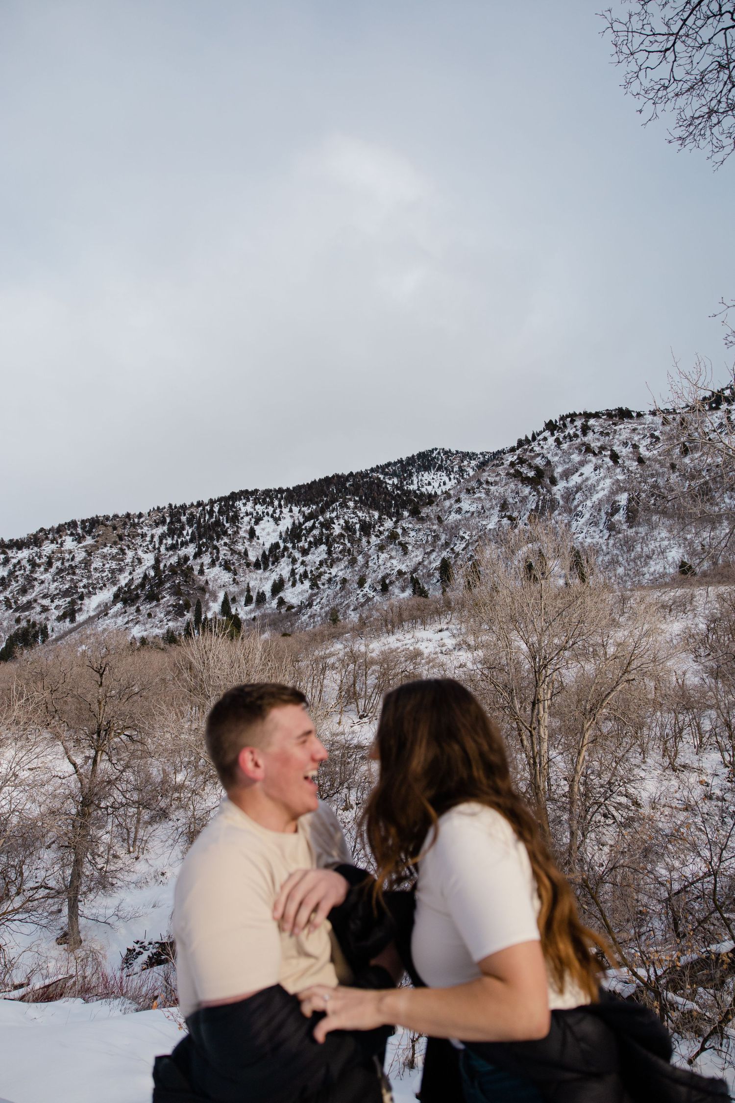 Sioux City, Iowa photographer. Happy couple laughing together in snowy mountain landscape under overcast winter sky.