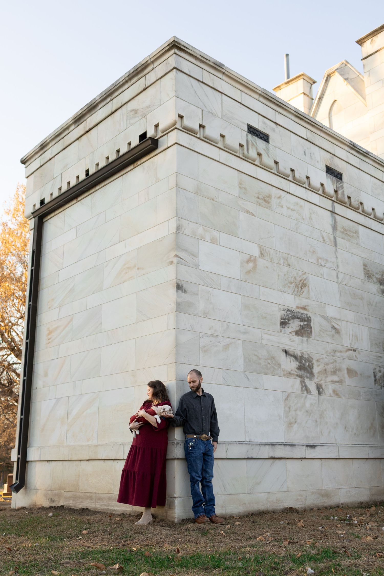Sioux City, Iowa photographer. A couple leans against the corners of a large white stone building outdoors during golden hour.