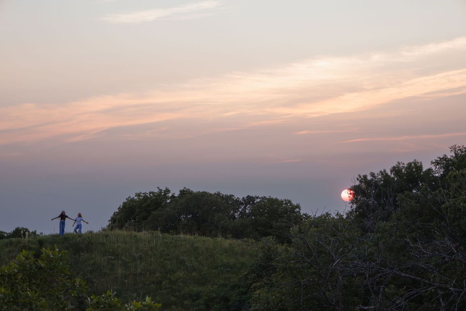 Sioux City, Iowa photographer. Silhouette of couple holding hands on hilltop at golden sunset with lush trees.
