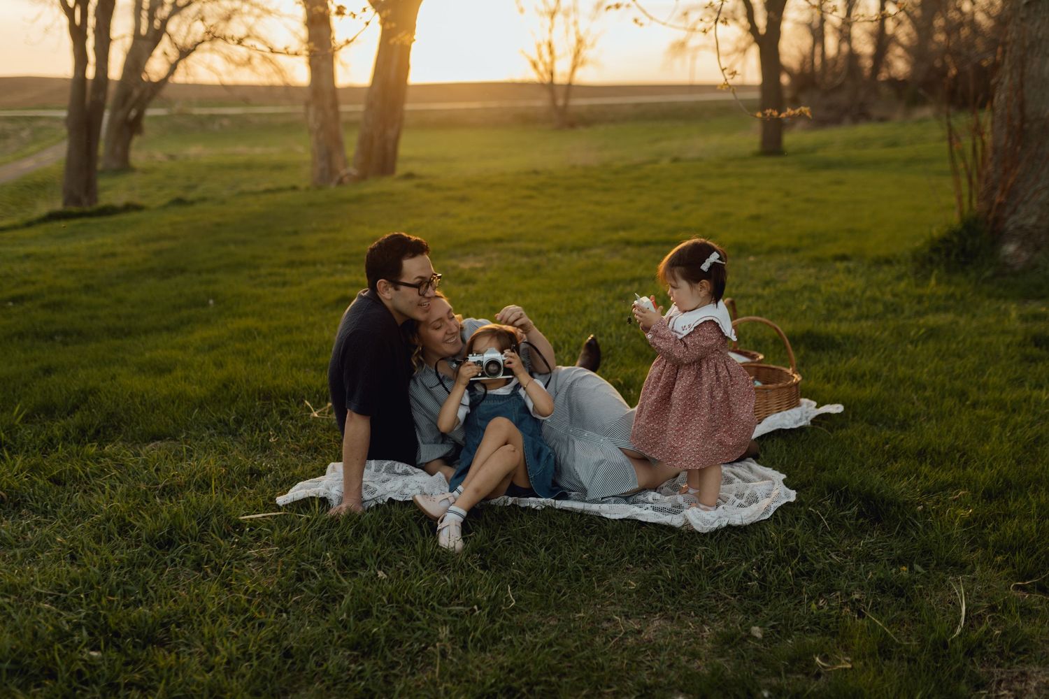 Sioux City, Iowa photographer. A family sits on a blanket in a grassy field at golden hour with two young children playing.