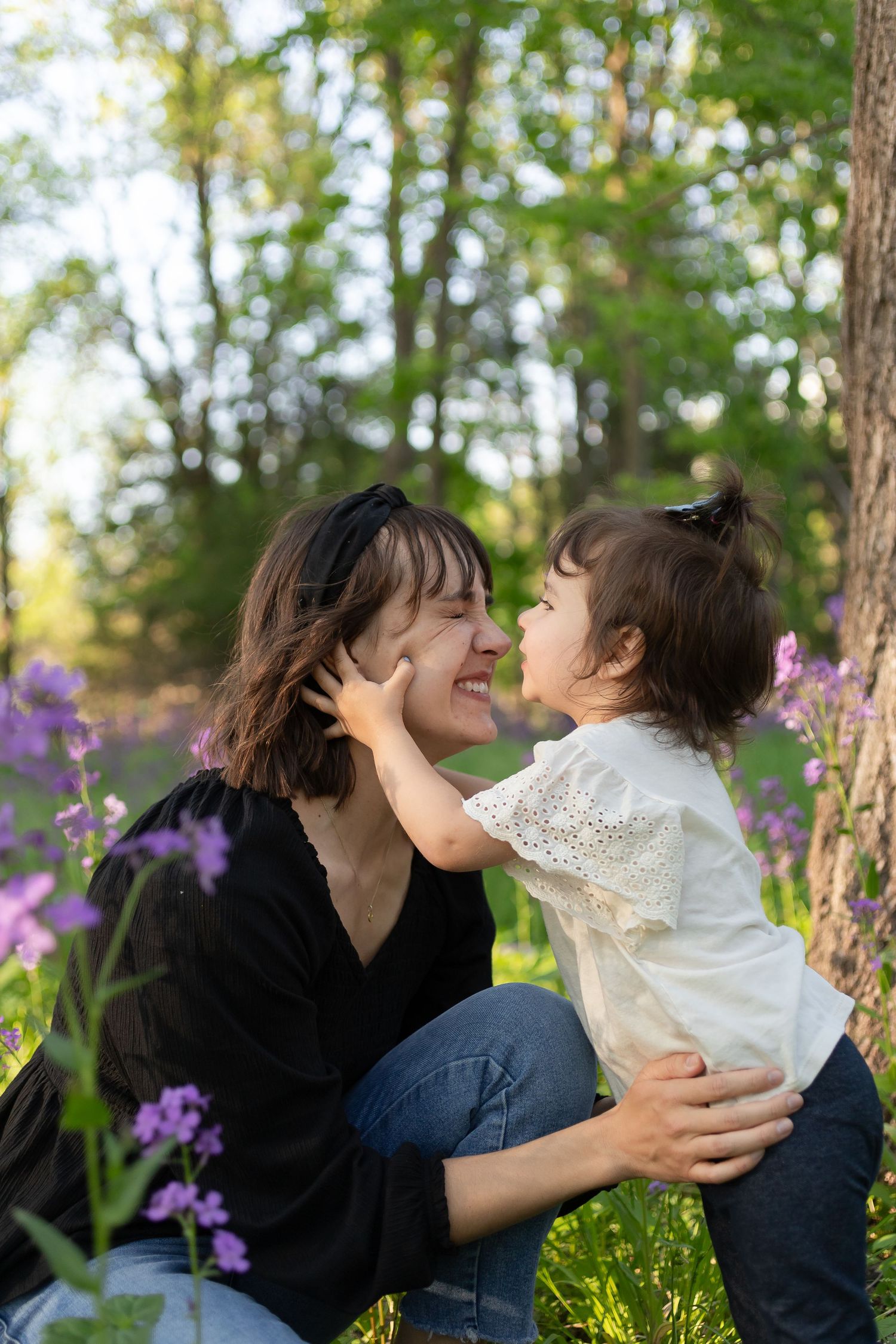 Sioux City, Iowa photographer. Joyful mother and toddler daughter sharing tender moment in sunny forest with purple blooms.