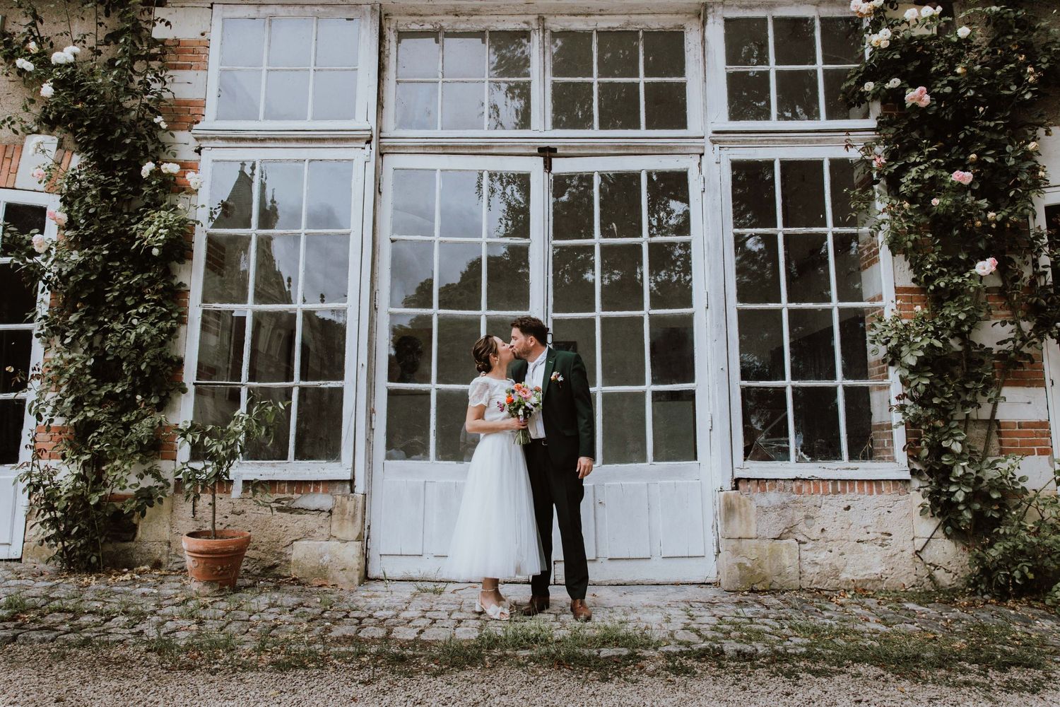 A panoramic view of five wedding moments captured in a series against a stone building with white glass doors and windows.