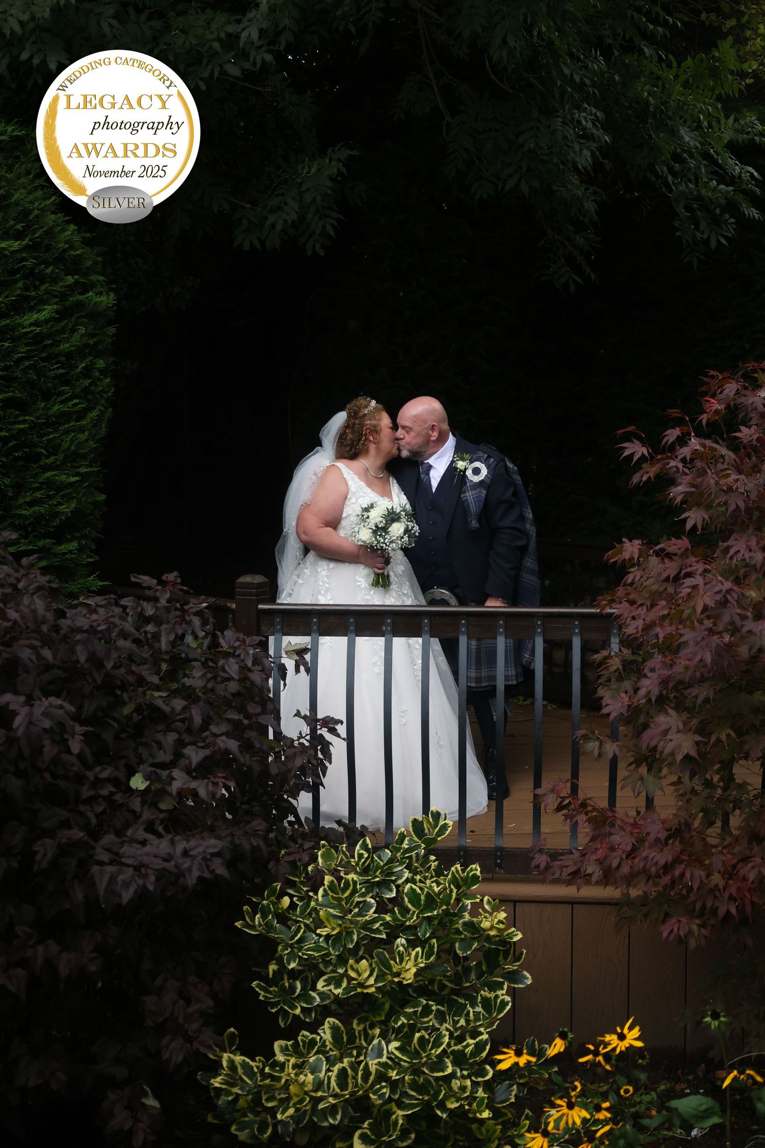 A romantic wedding couple shares an intimate moment on a garden balcony surrounded by lush greenery and flowers.