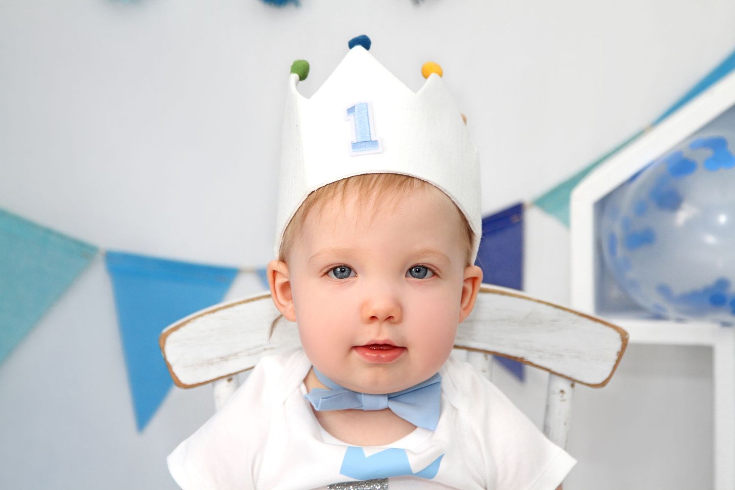 A baby wearing a white chef's hat and apron smiles while sitting in a kitchen setting.