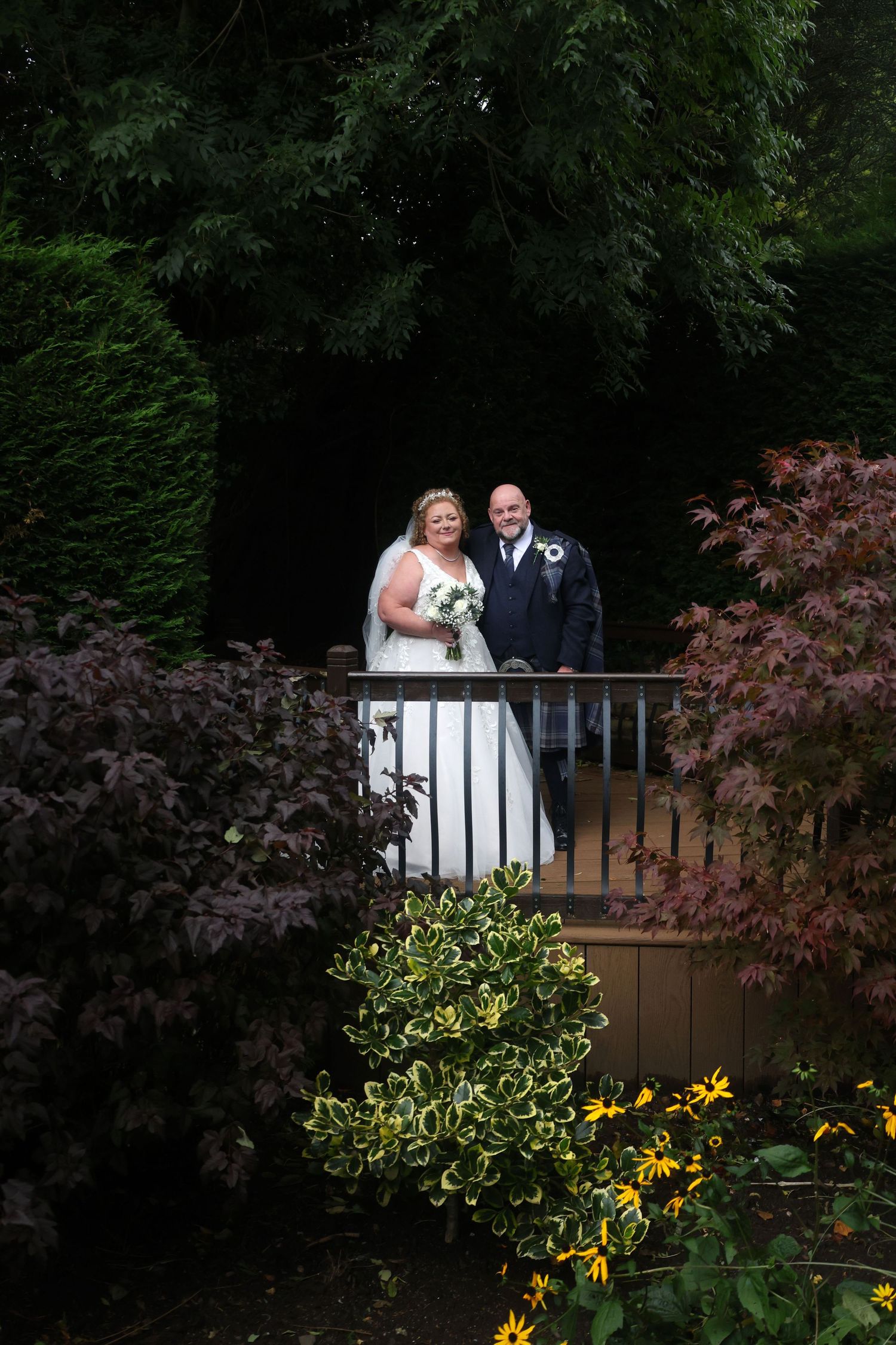 Bride and groom posing on a garden balcony surrounded by lush greenery and colorful autumn foliage on their wedding day.