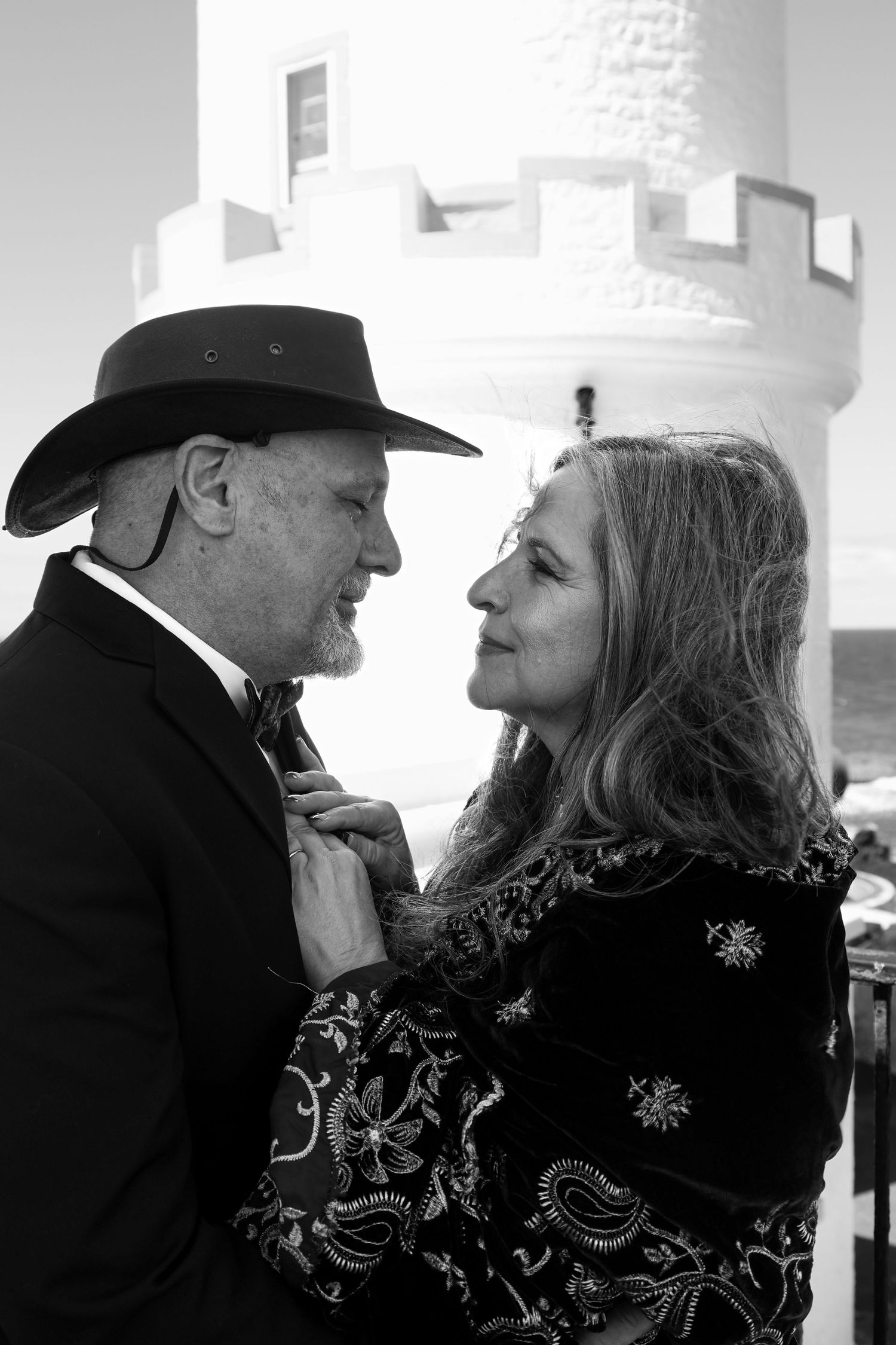 Black and white photo of a couple in formal attire sharing a romantic moment near a lighthouse.R.A.M Photography, Stranraer
