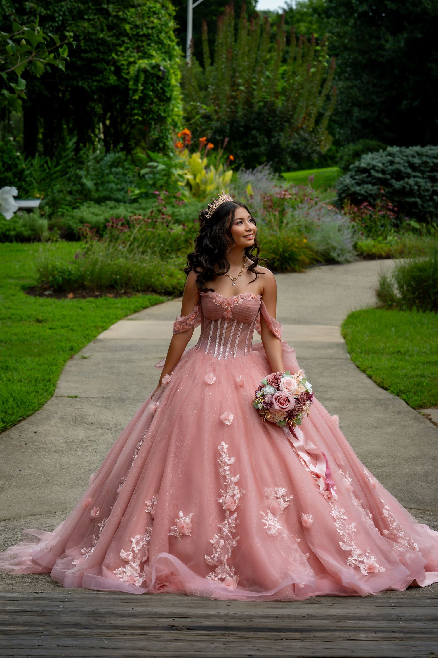 A stunning pink ball gown with floral appliques and a sweetheart neckline photographed in a lush garden setting.