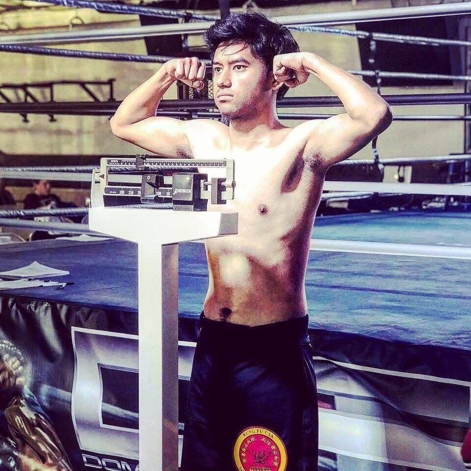 Athletic young male boxer flexes muscles during a weigh-in beside a scale in a boxing ring.