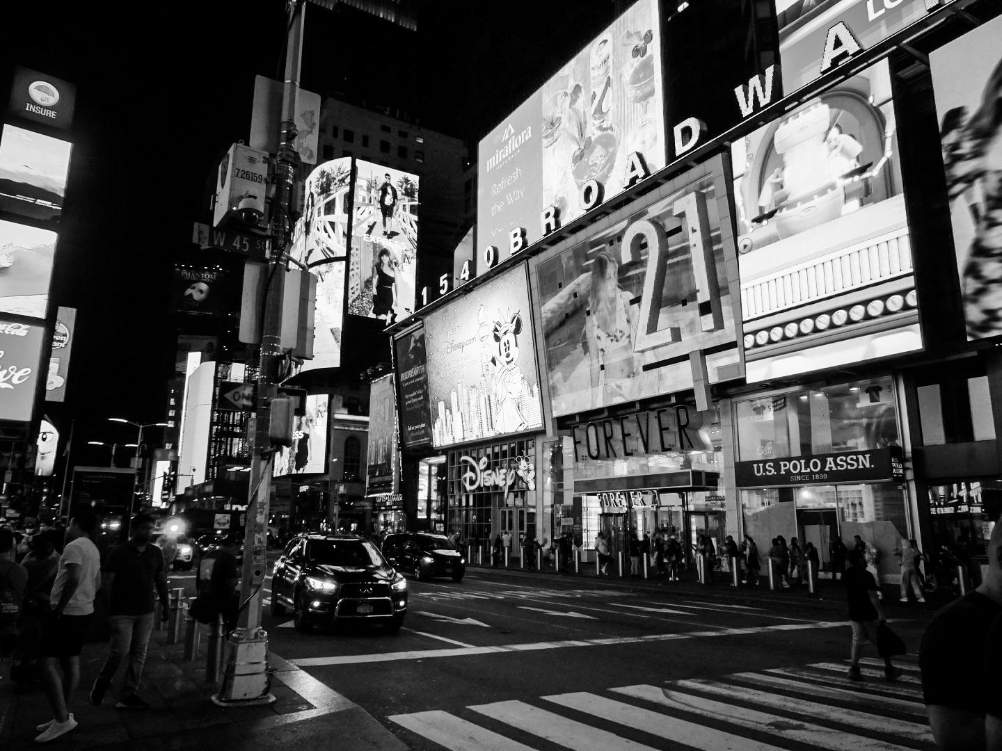 A bustling Times Square at night with bright billboards and city traffic in black and white.