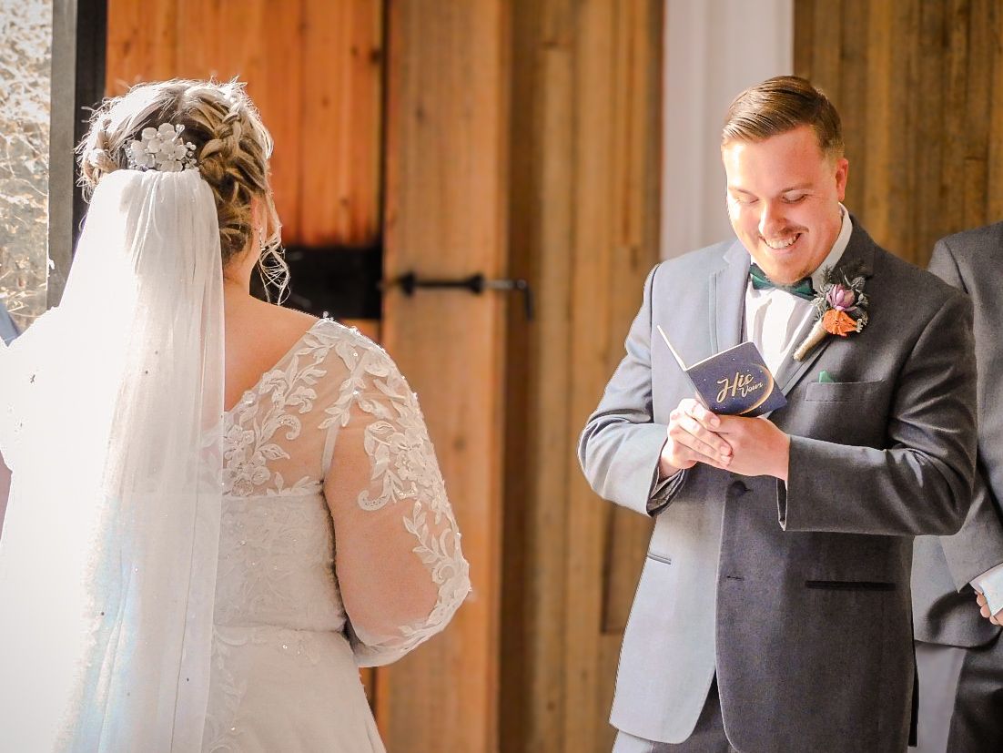 Groom smiling while reading wedding vows to bride during an intimate rustic barn wedding ceremony.