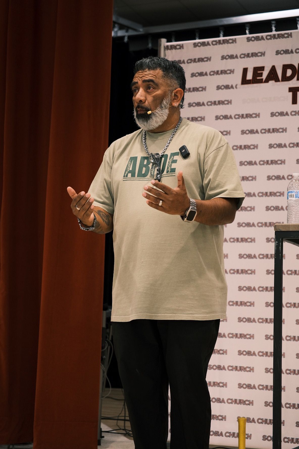 Bearded man in ABOVE t-shirt speaking at Sobia Church leadership conference.