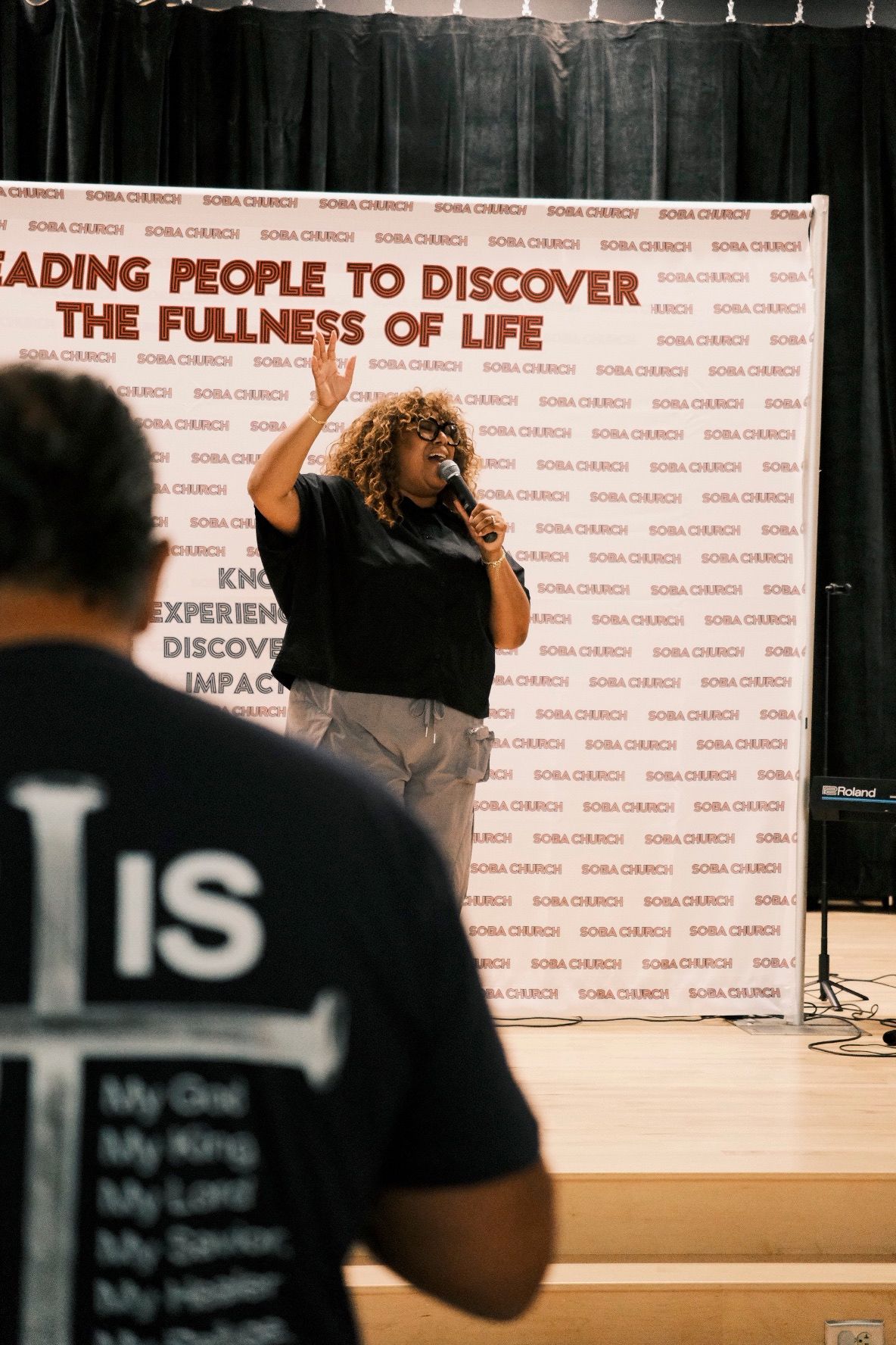 Woman singing on stage with microphone at Boba Church fullness of life event.