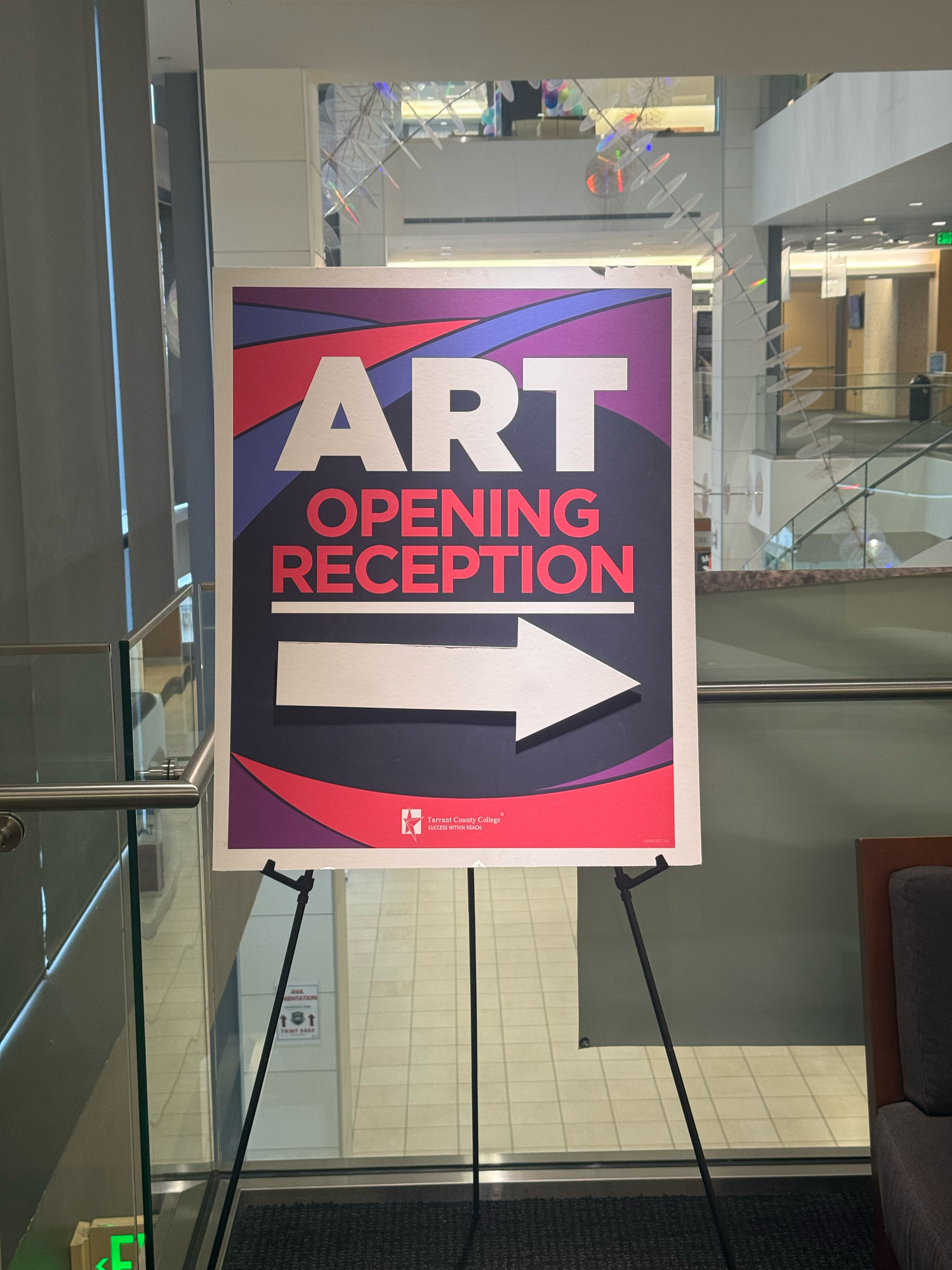 Art Opening Reception directional sign on an easel inside a modern building atrium.
