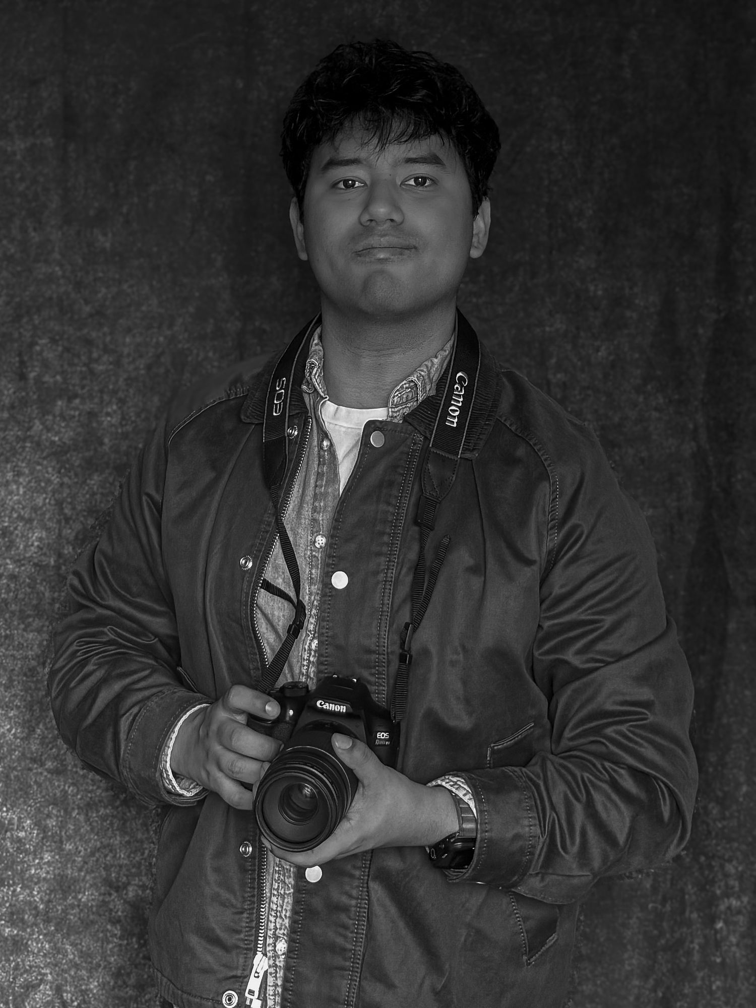 Young man holding a Canon DSLR camera poses for a black and white portrait photography shot.