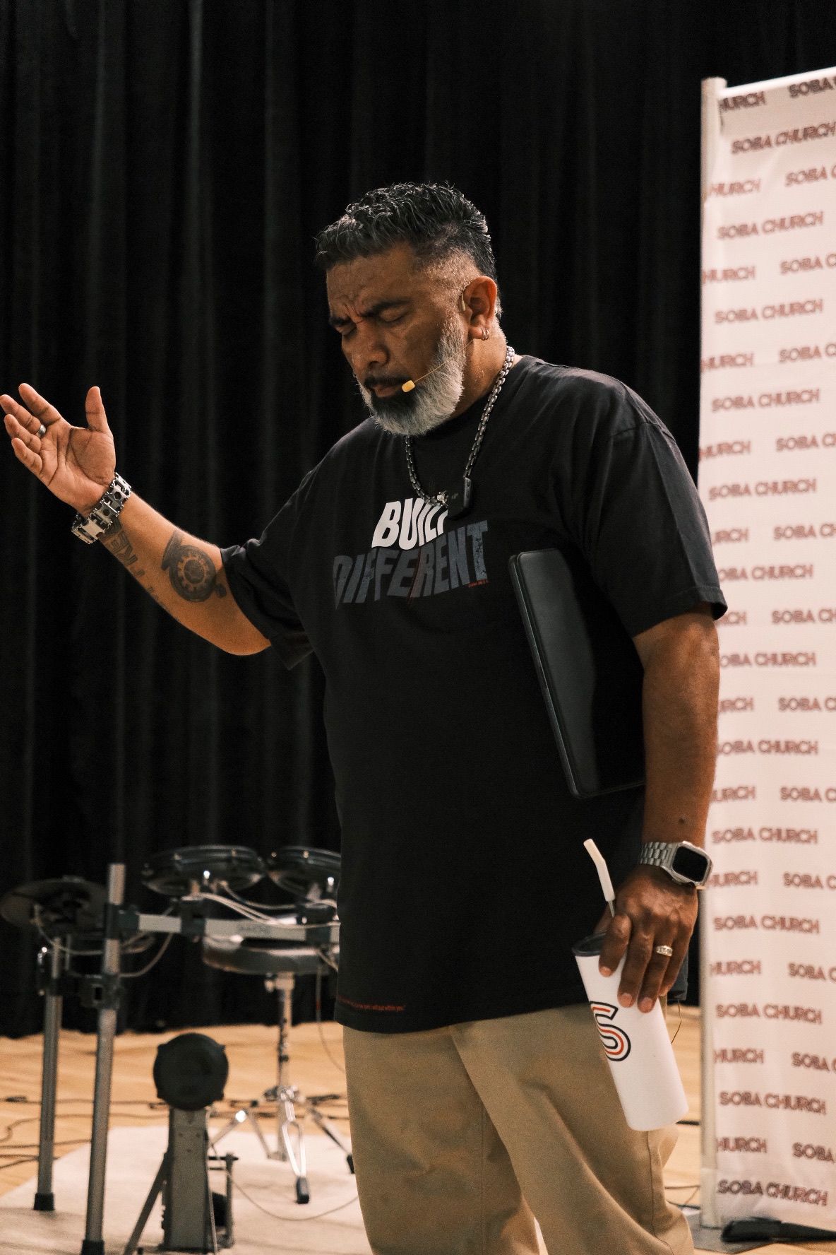 Man in black t-shirt speaking on stage at Boba Church event.