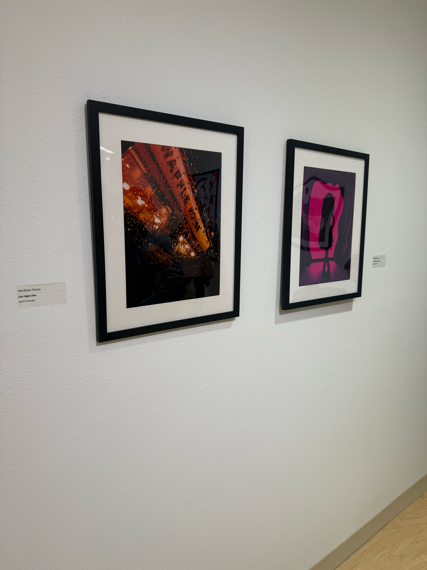 Two framed photographs displayed on a white gallery wall, featuring vibrant red and pink artistic images.