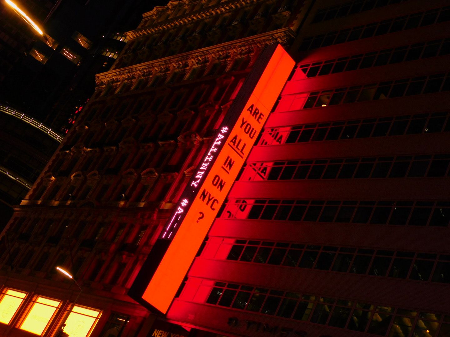 Red illuminated building facade at night displaying bold text signage in an urban city setting.