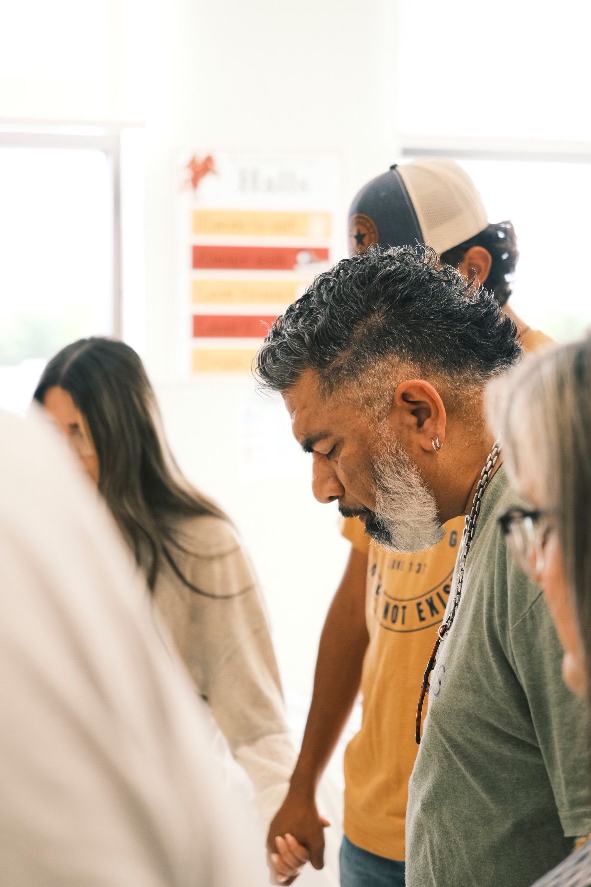 Man with gray beard bowing head in prayer during church group gathering.