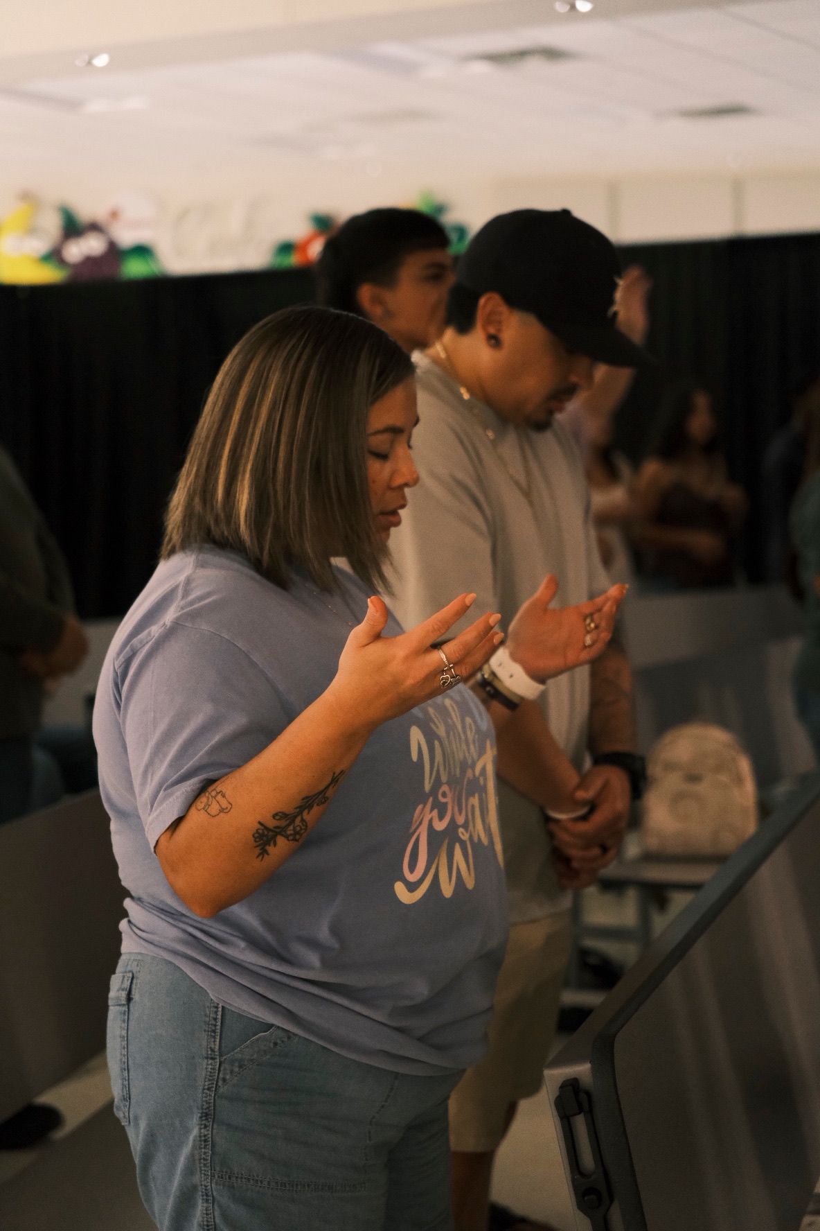 Woman in gray t-shirt praying with hands raised at Sobia Church worship service.