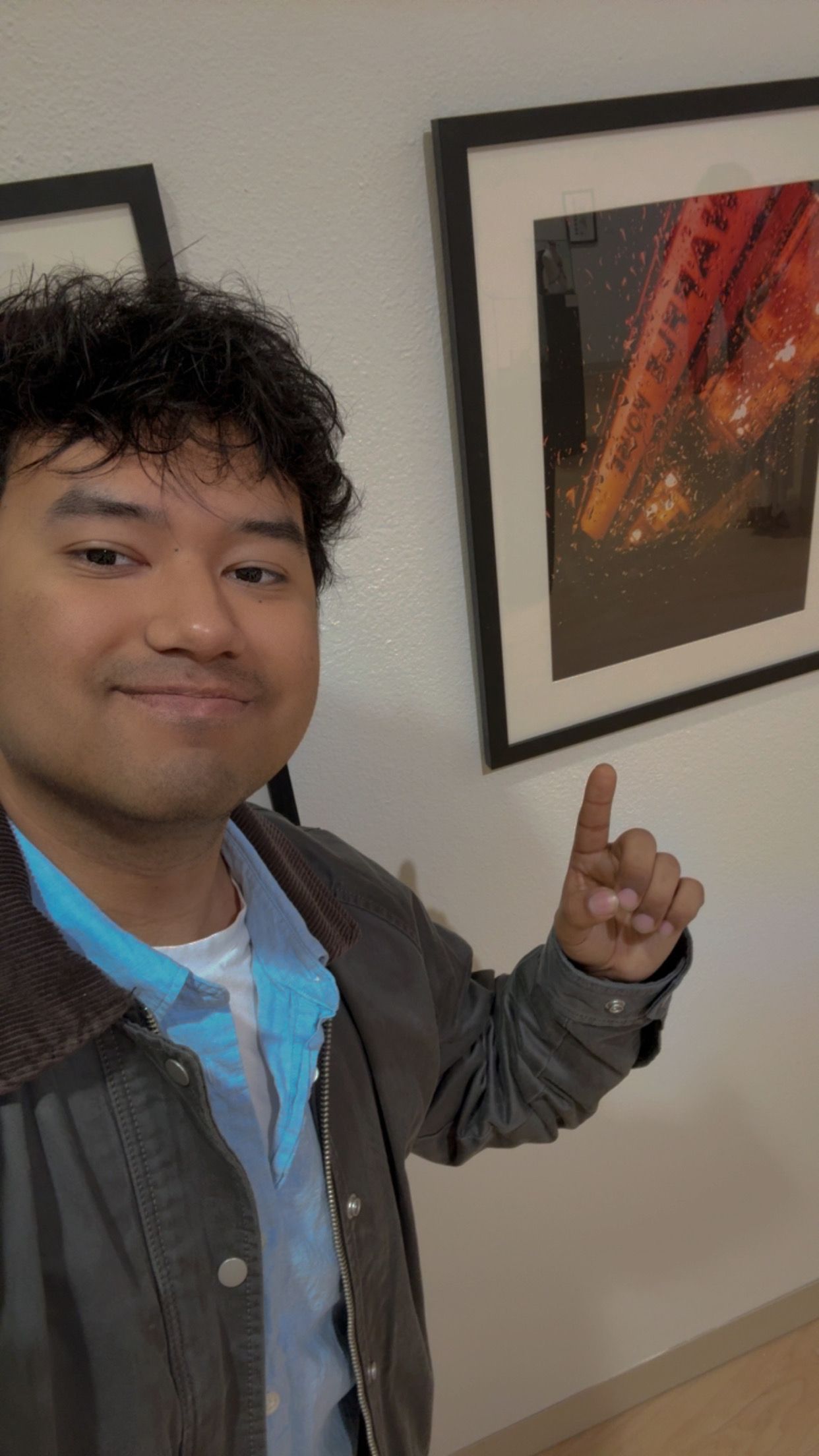 Young man points proudly at his framed red-toned photograph displayed on a gallery wall.