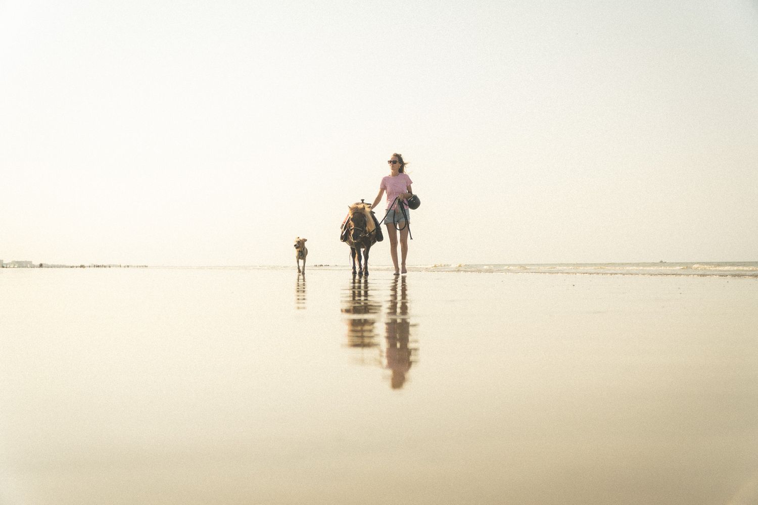 Mother and children walking on a reflective wet beach at sunset.