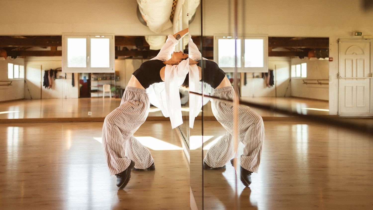 Dancer in white outfit performing a split against a mirror in a bright dance studio.