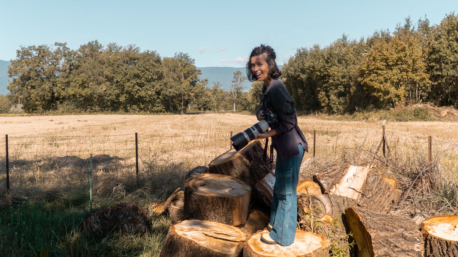 Photographe professionnelle debout sur des souches de bois en train de viser dans la campagne