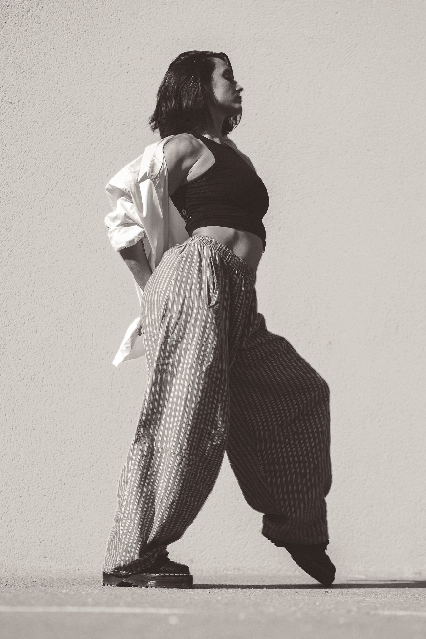 A woman in striped wide-leg pants and crop top poses against a wall in black and white.