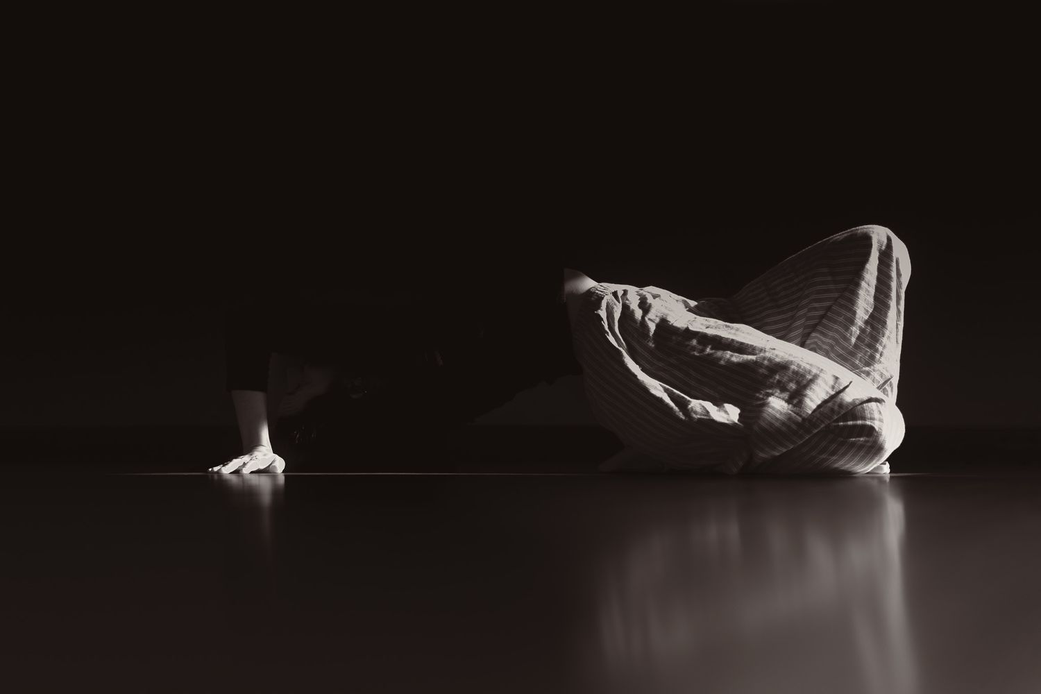 Black and white photo of a person in martial arts uniform bowing low to the floor in darkness.