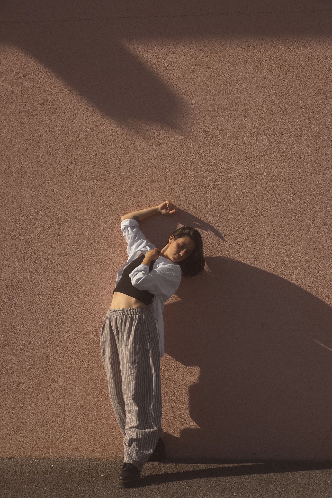 Female dancer leaning against a terracotta wall with dramatic shadows in urban setting.