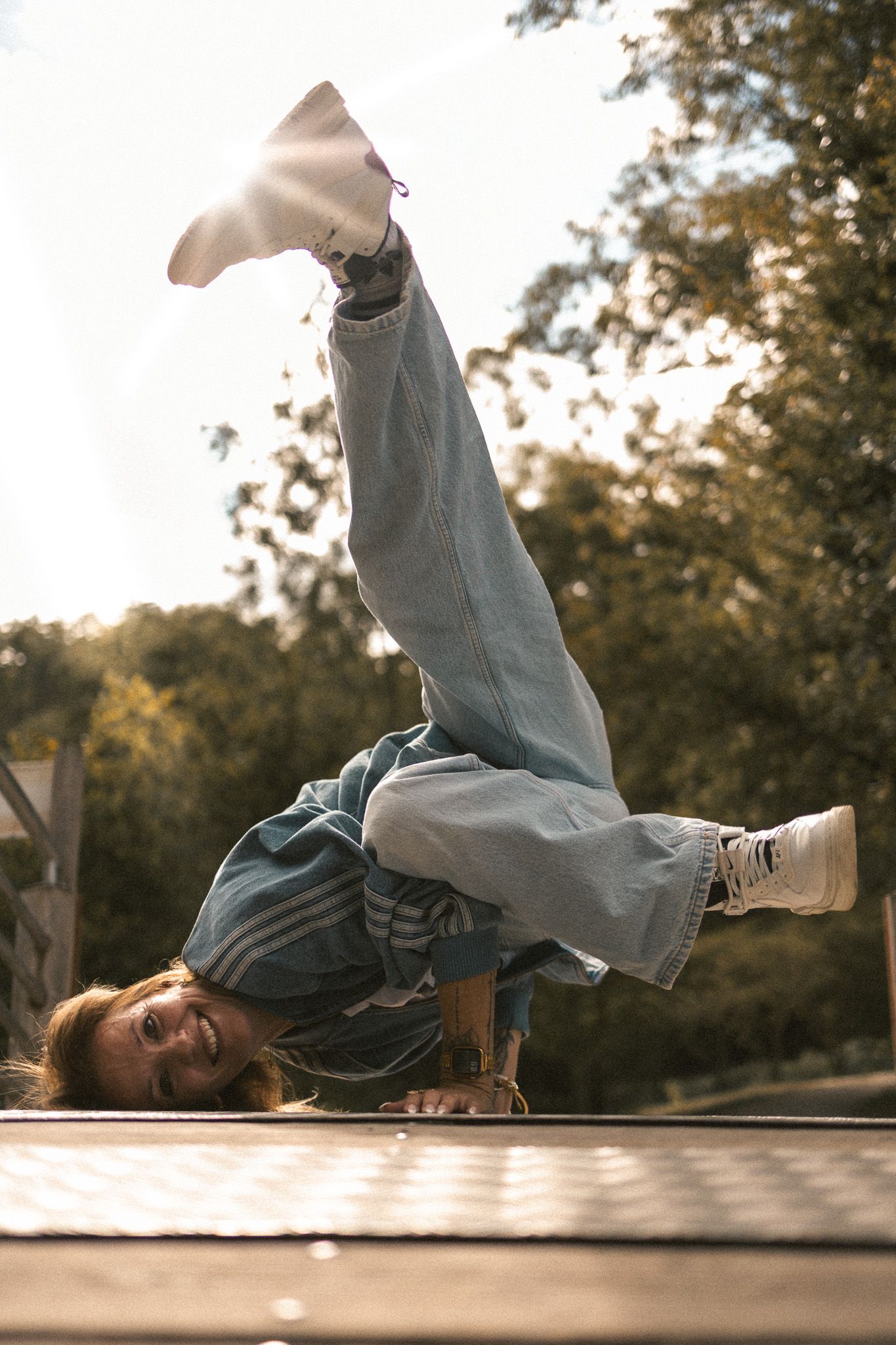 A breakdancer performs a headstand with legs raised on a metal surface outdoors in sunlight.