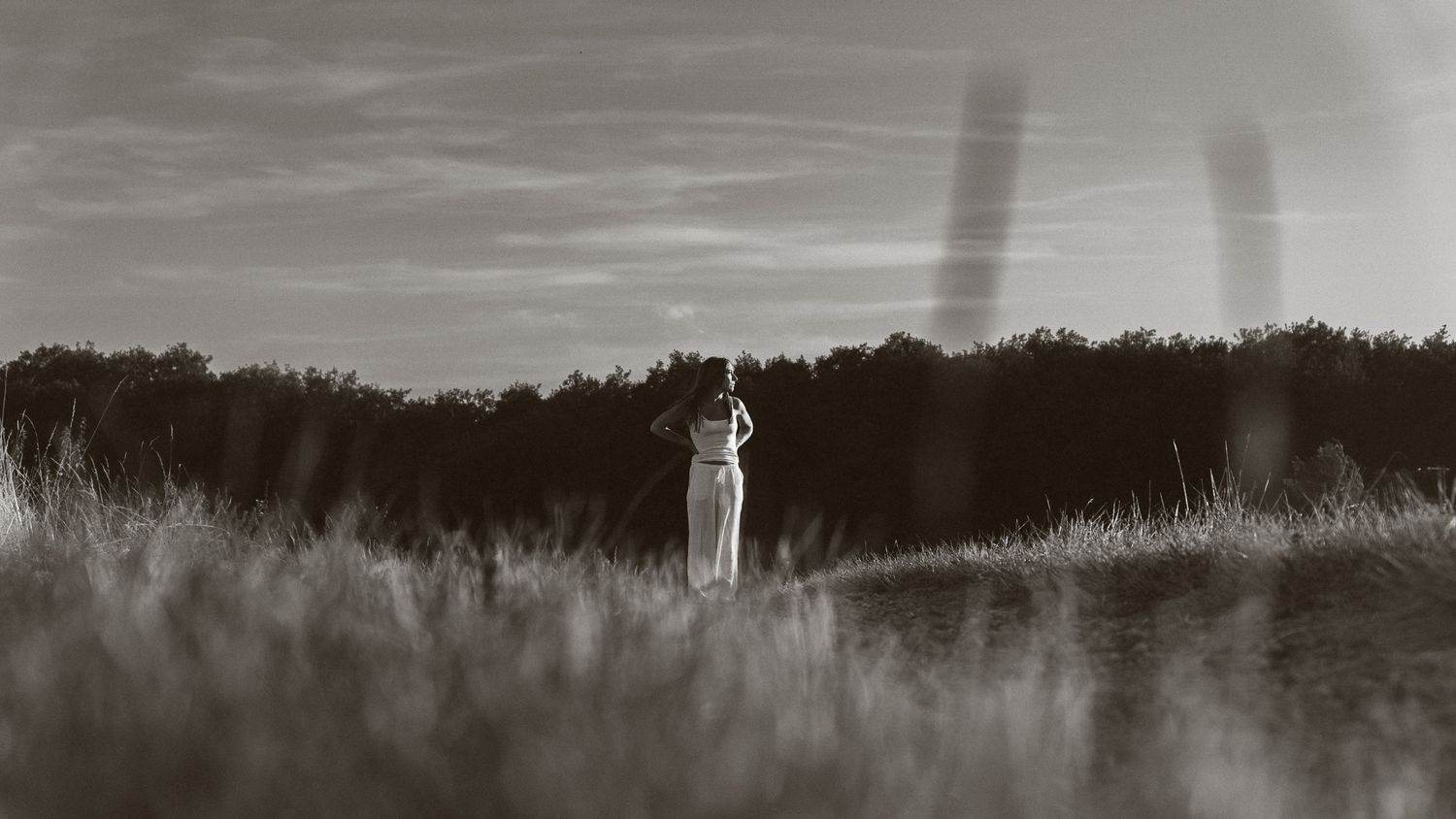 Black and white photo of a lone figure standing in a field, arms raised, with shadowy silhouettes looming behind.