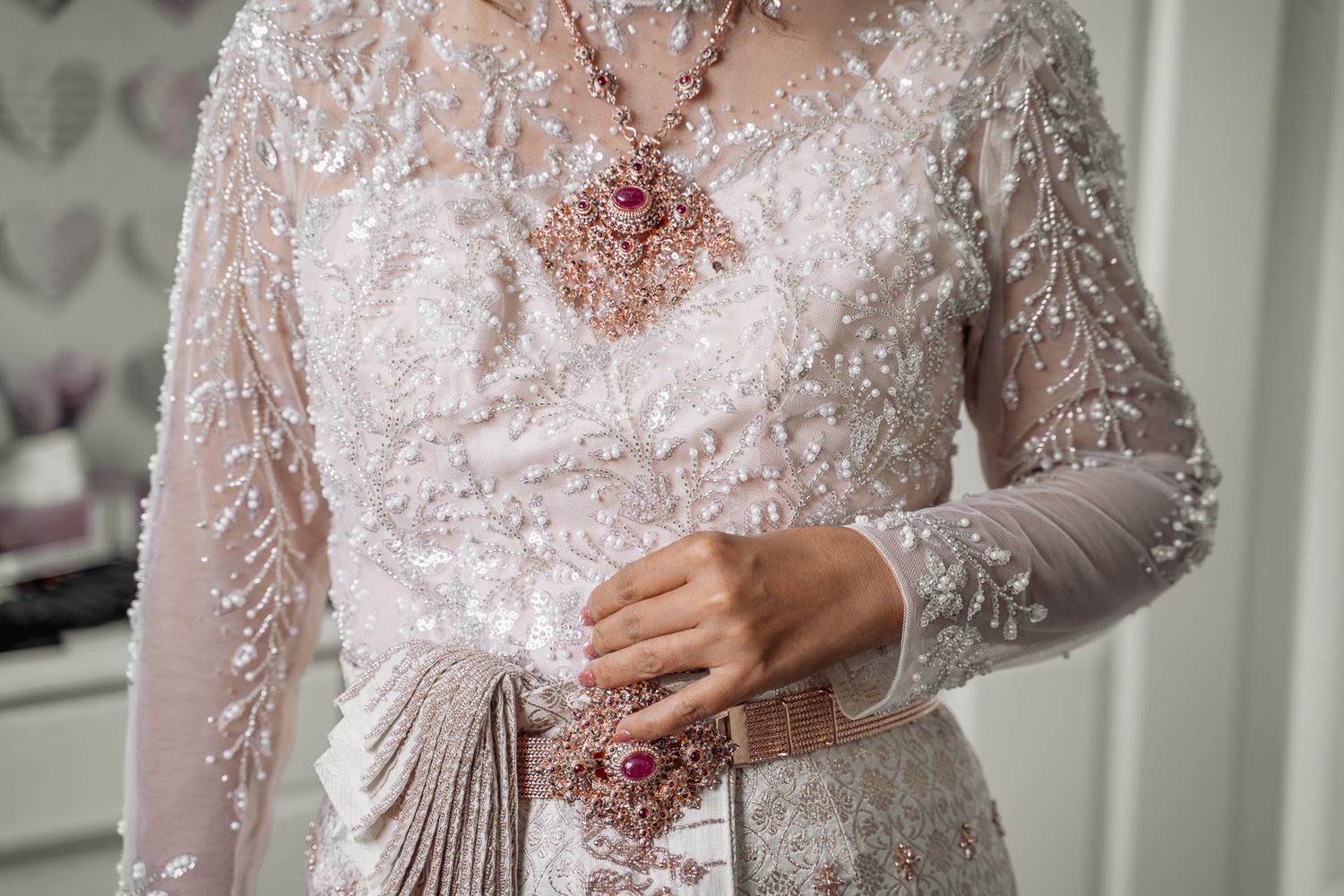 A bride wearing an ornate white beaded kebaya gown with a ruby gemstone necklace and matching ring at Lazaat Hotel, Cottingham, Hull