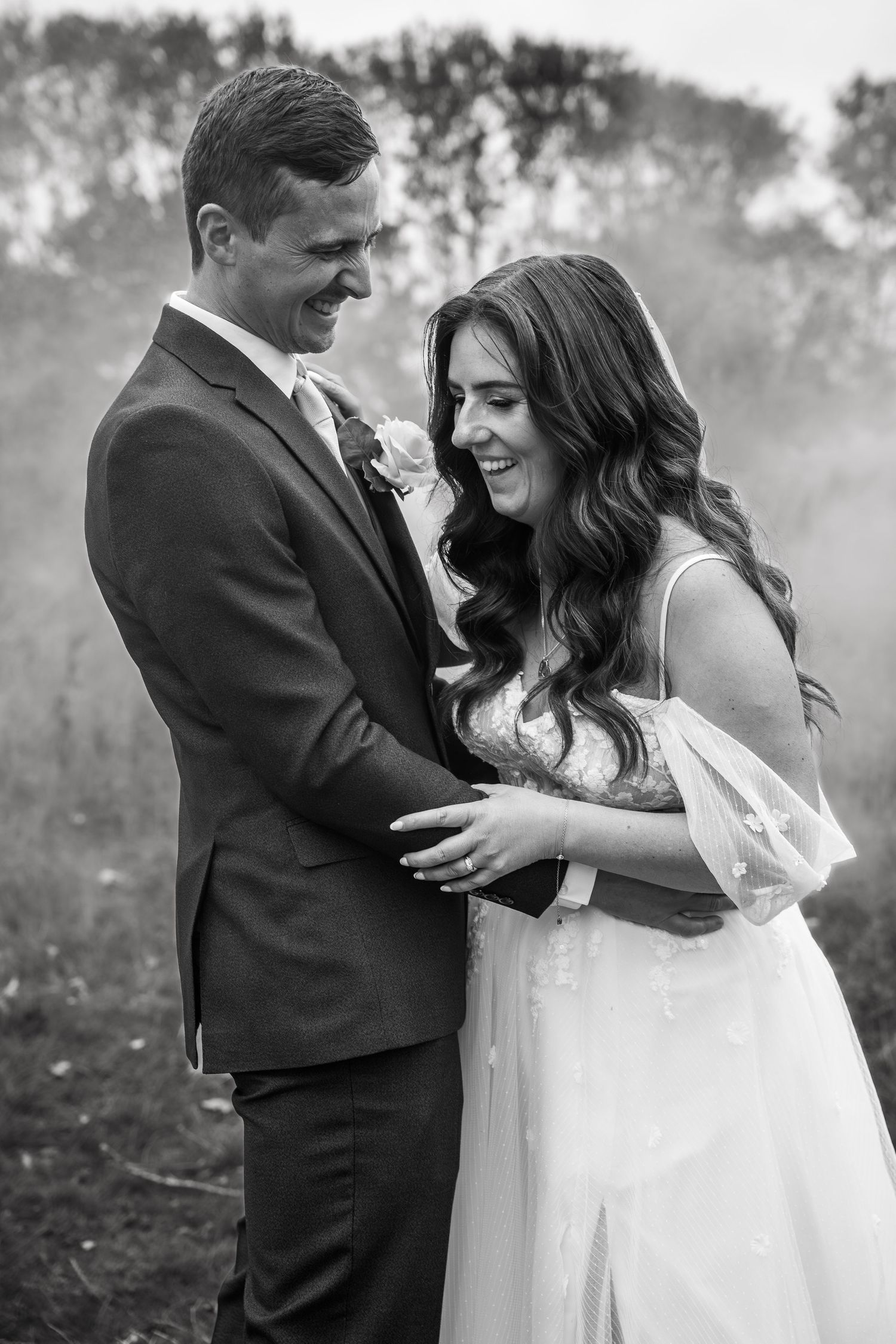 Black and white photo of smiling bride and groom embracing in misty outdoor setting.