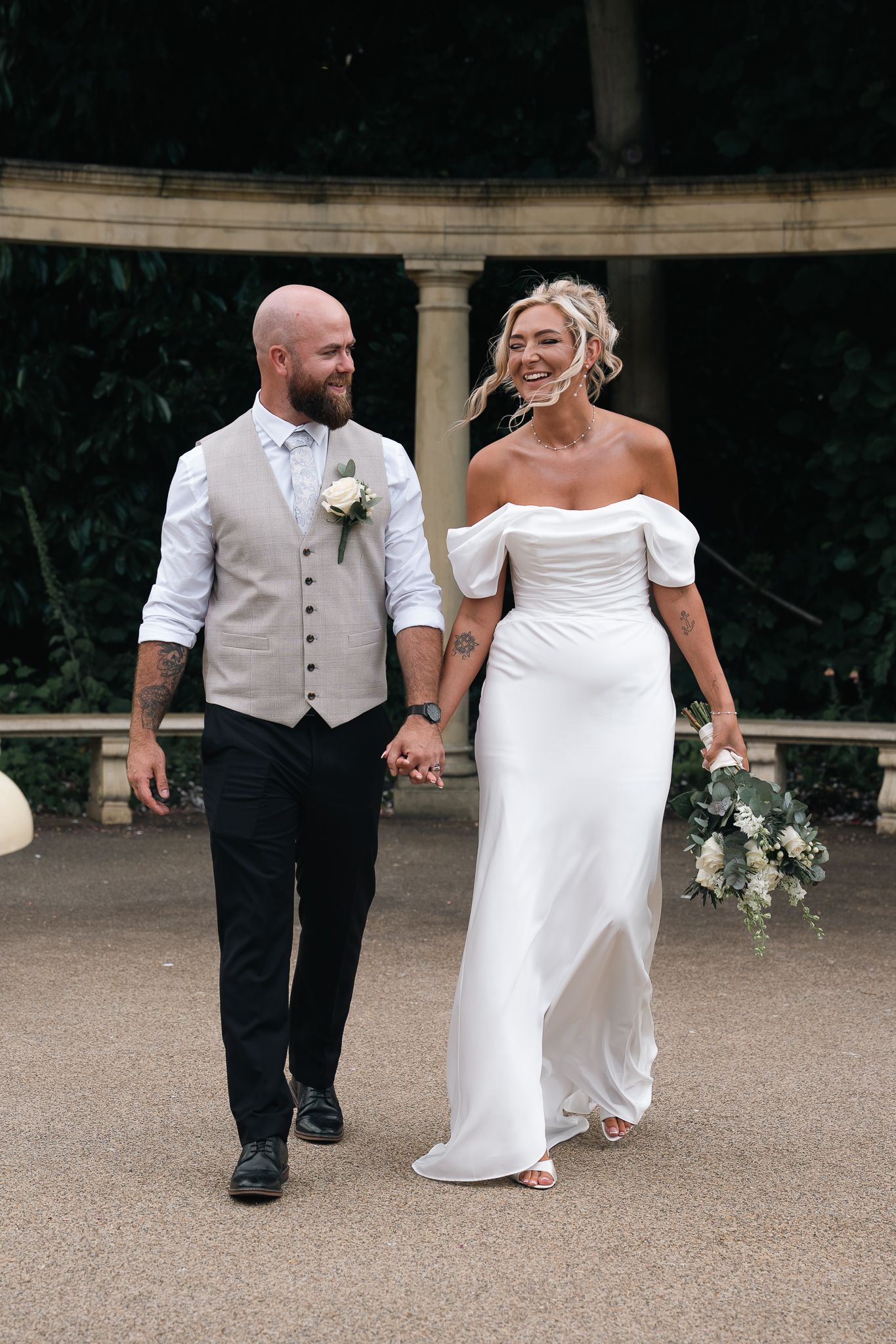 Smiling bride and groom walking hand in hand outdoors at elegant venue.