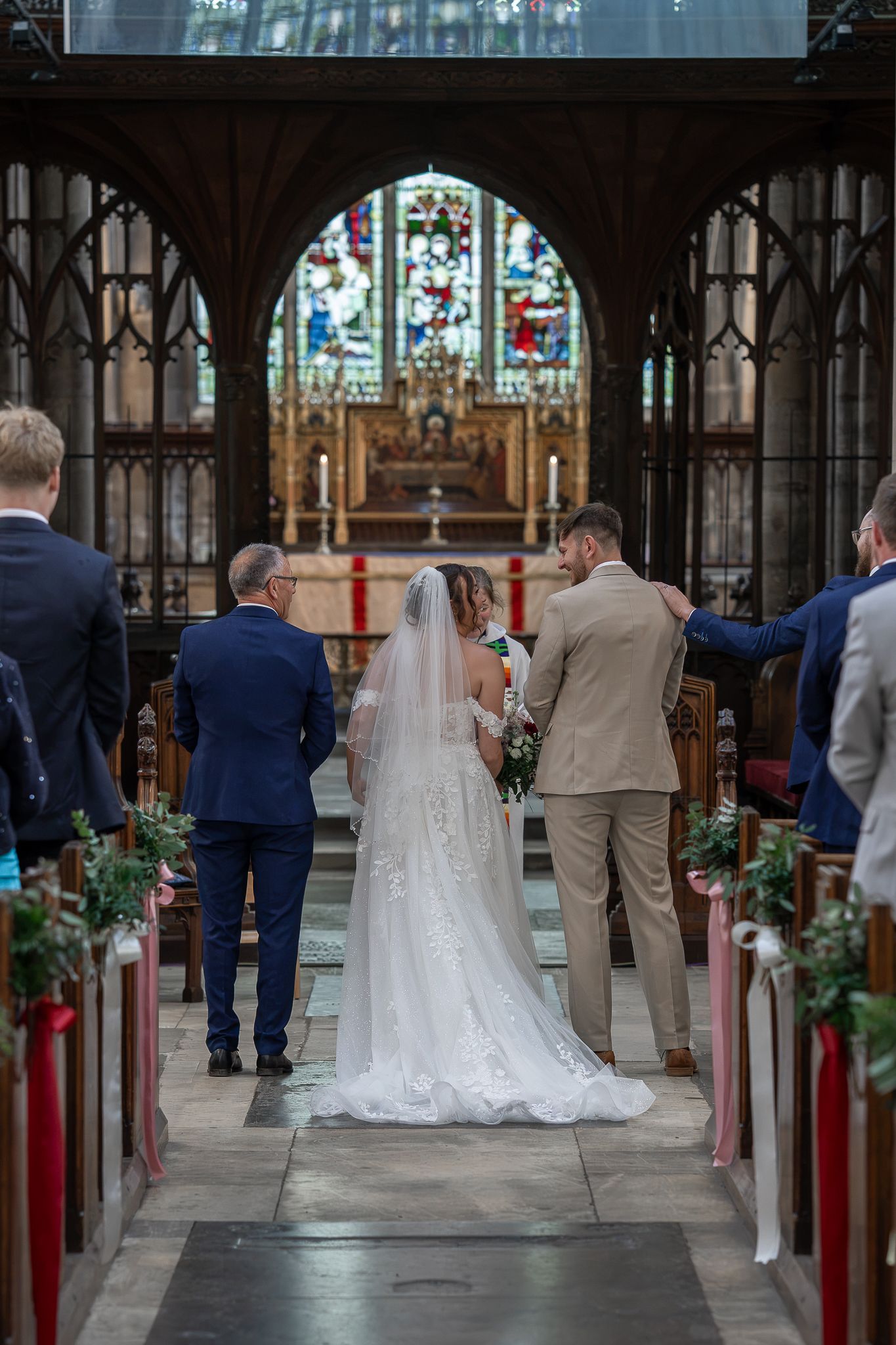 Bride and groom standing at the altar of a historic church with stained glass windows.
