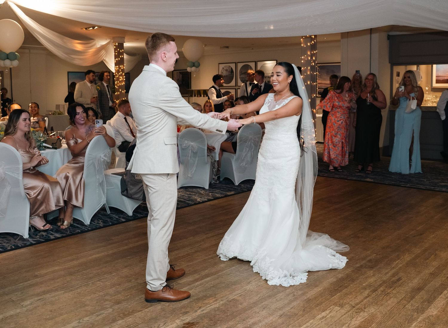 Newlywed couple shares first dance at elegant wedding reception with guests watching.