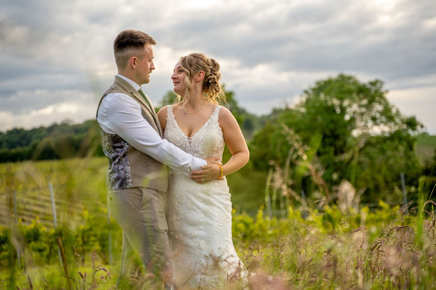 Bride and groom sharing a romantic embrace in a lush green countryside wedding portrait.