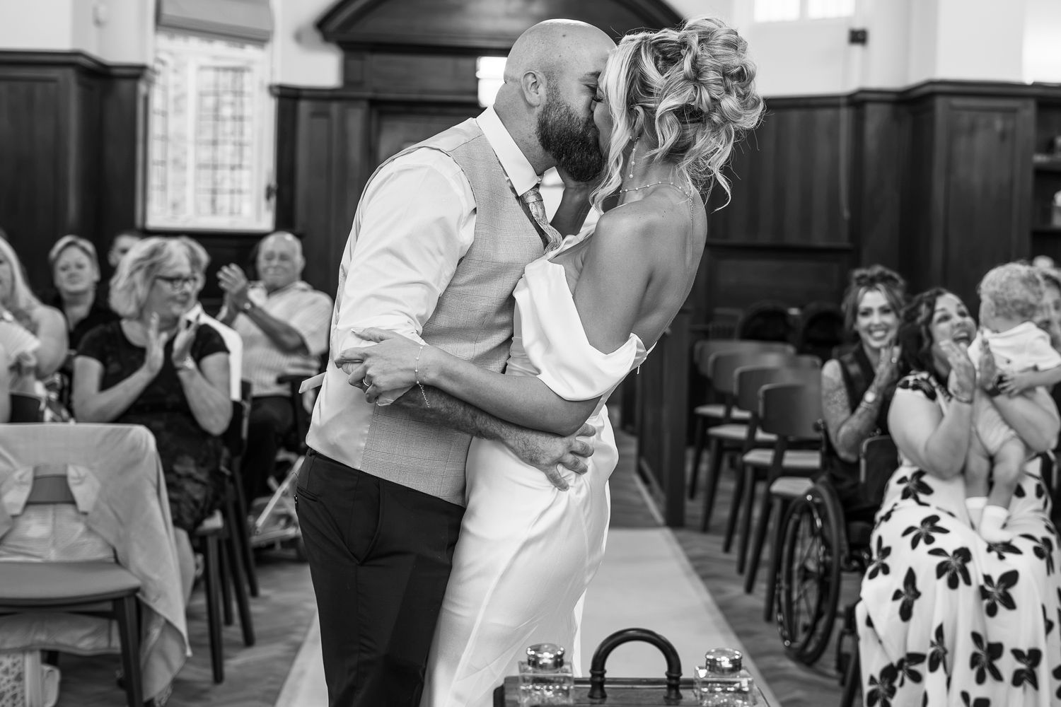 Black and white photo of bride and groom sharing first kiss at altar.