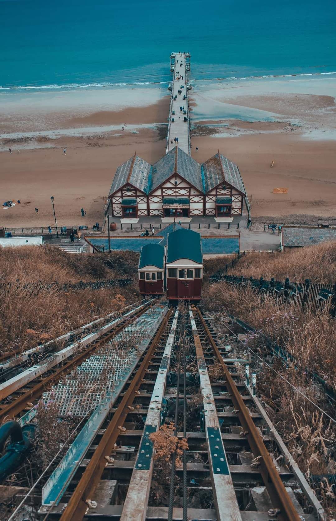 A vintage funicular railway car on tracks leading to a seaside pier and sandy beach.