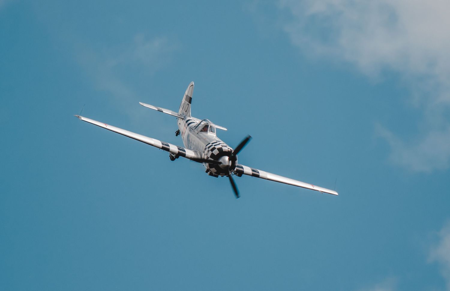 Vintage World War II propeller aircraft flying against a bright blue sky with clouds.