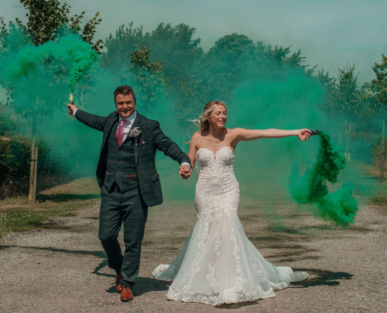 Bride and groom celebrating with green smoke bombs on a country path at wedding.