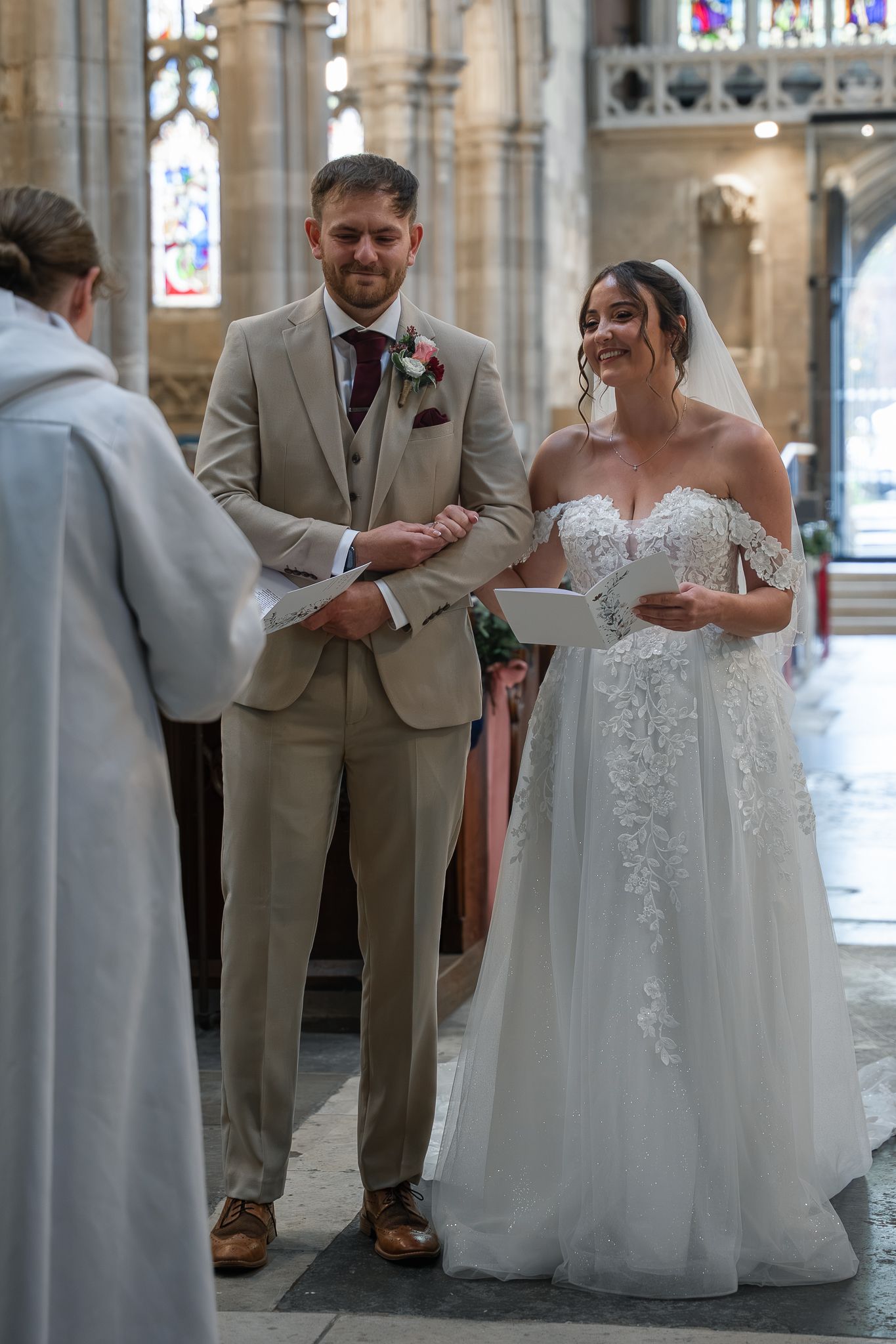 Bride and groom exchanging vows at a church wedding ceremony with stained glass windows.
