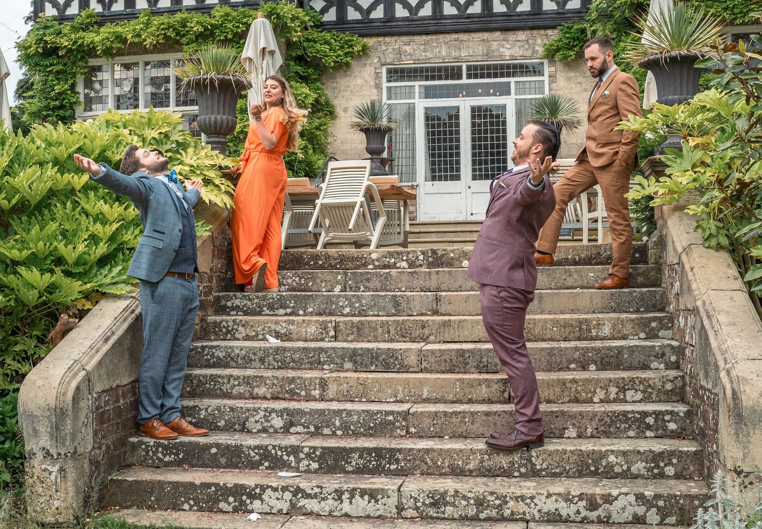 Four guests posing playfully on stone steps outside an ivy-covered country house venue.