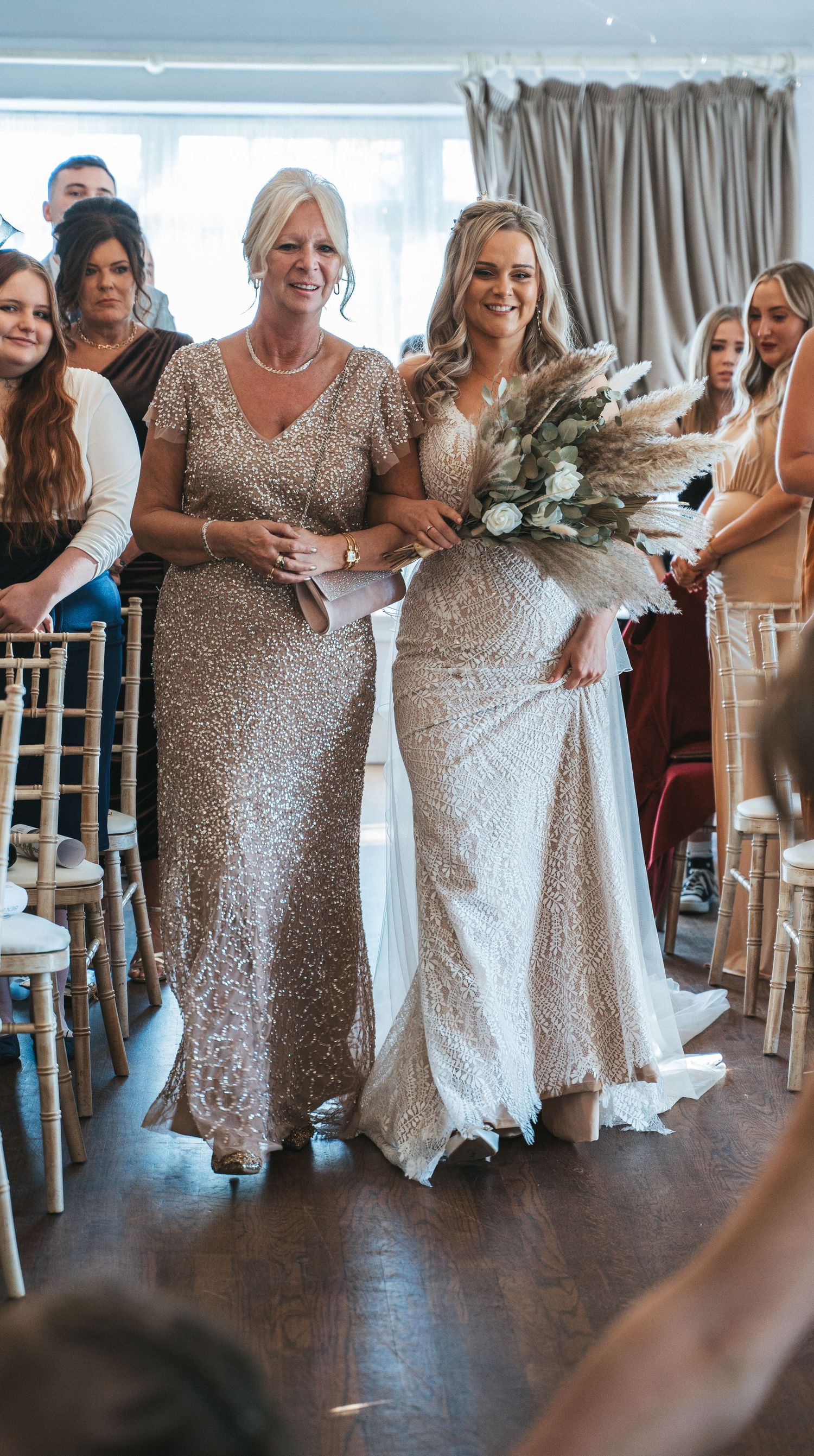 Bride walking down the aisle in a sequined gown with her mother at an elegant wedding ceremony.
