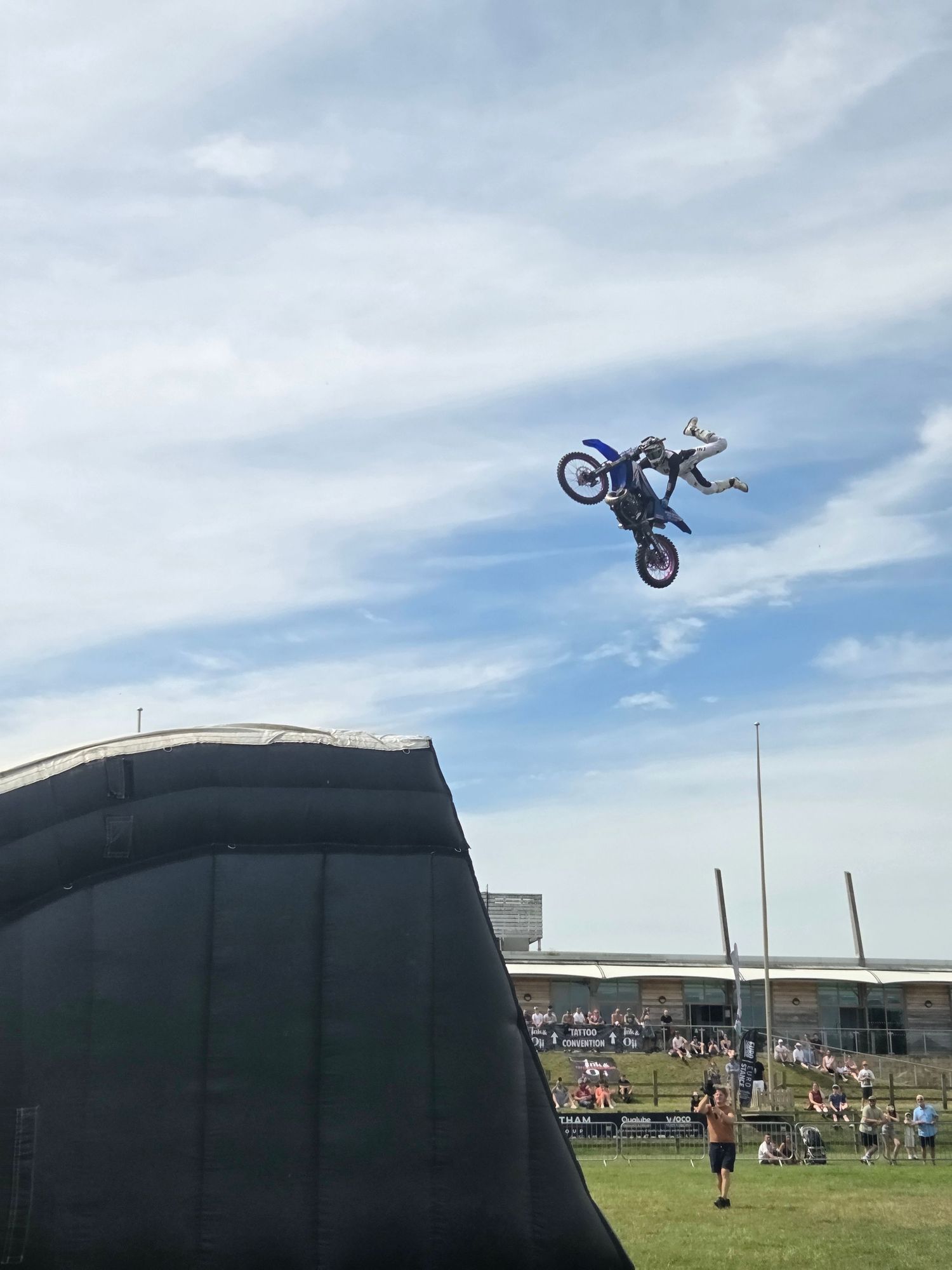 Motocross rider performing a high-flying aerial trick on a blue dirt bike at an outdoor stunt show.