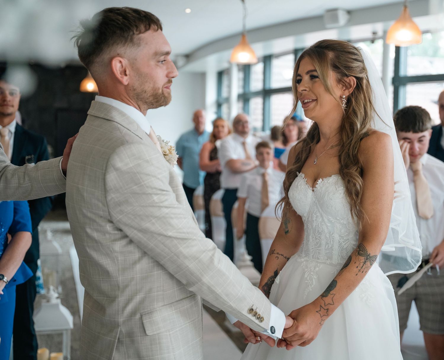 Bride and groom holding hands and smiling during their wedding ceremony indoors.
